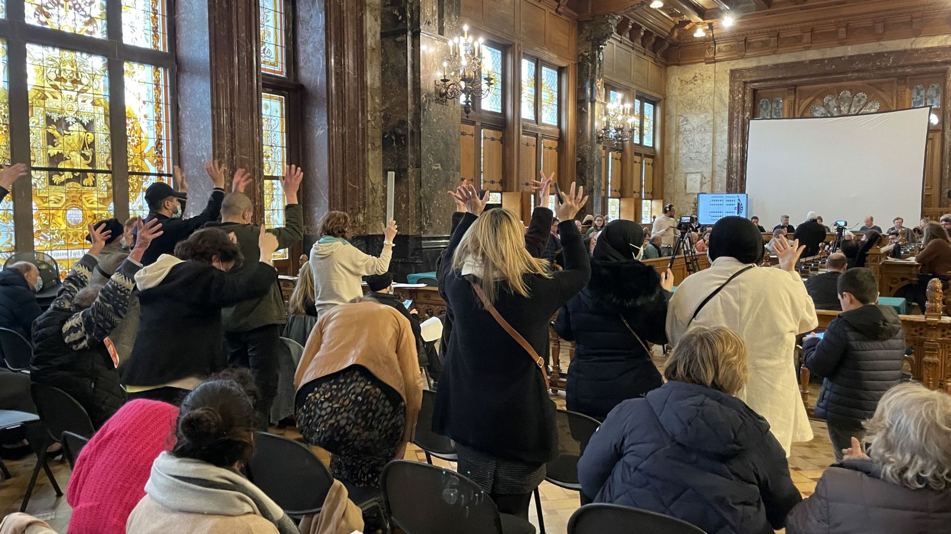 Le public proteste silencieusement lors du conseil communal de Schaerbeek du 29 mars en adoptant les applaudissements de la langue des signes.
