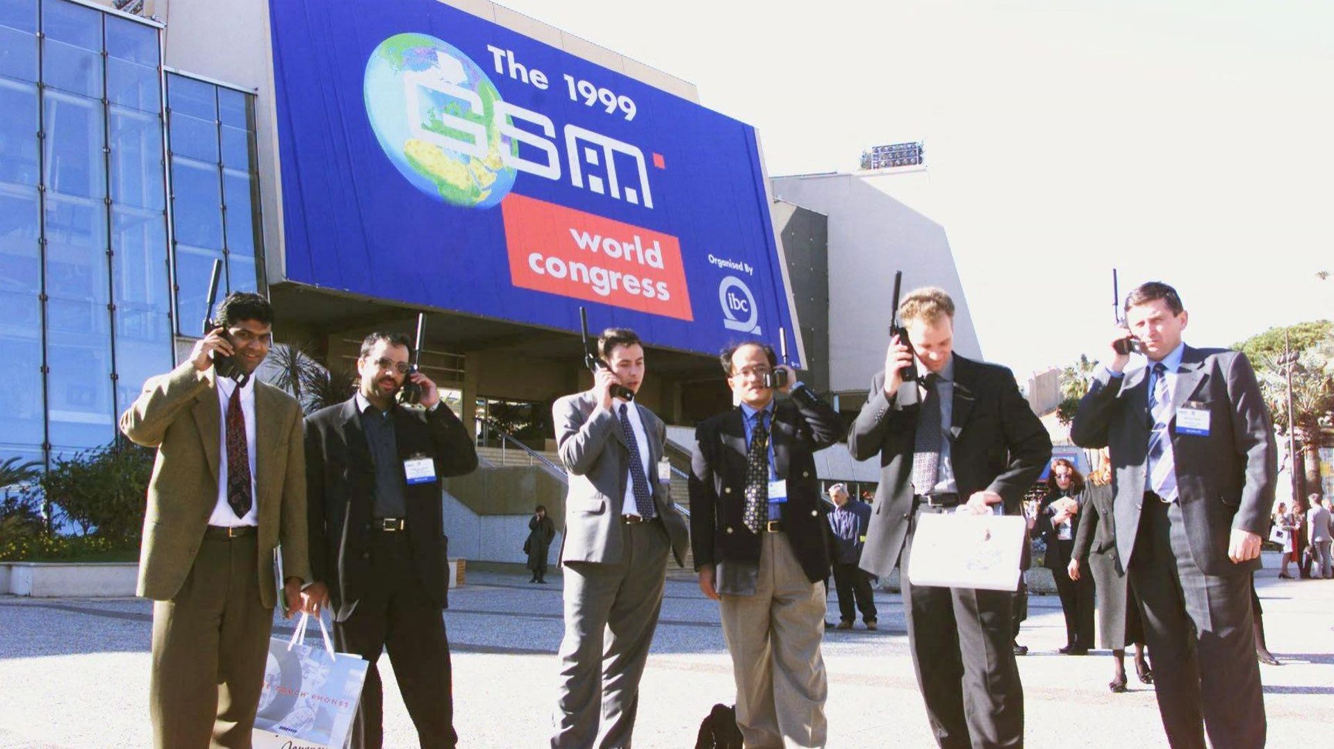 Six hommes d'affaires utilisent un téléphone portable en 1999, lors du salon du GSM à Cannes.
