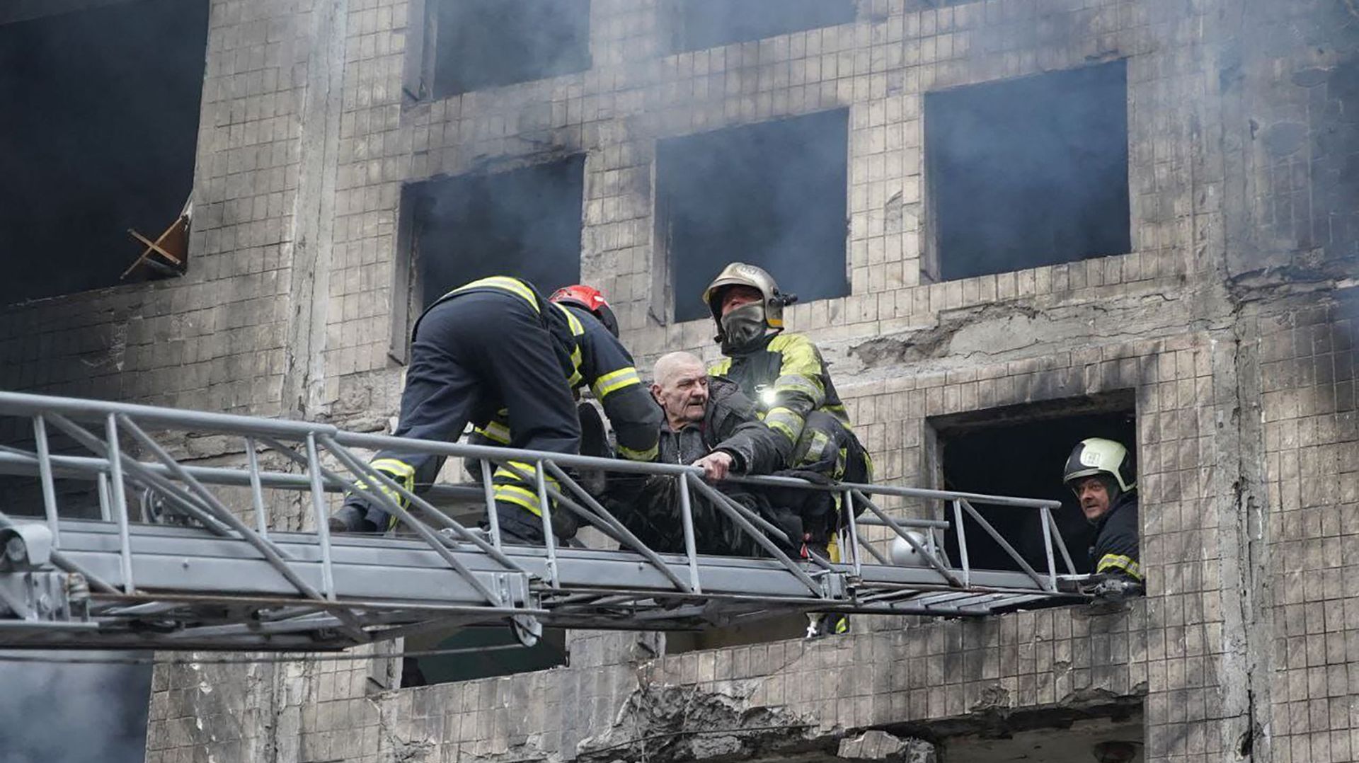 Sur cette photo prise et publiée par le service d'urgence de l'Ukraine le 14 mars 2022, des pompiers évacuent un homme d'un immeuble d'habitation touché par un bombardement dans le quartier d'Obolon à Kiev.