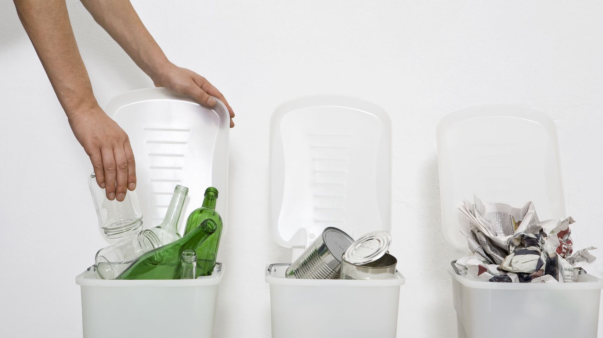A human hand putting a glass jar in a recycling bin
