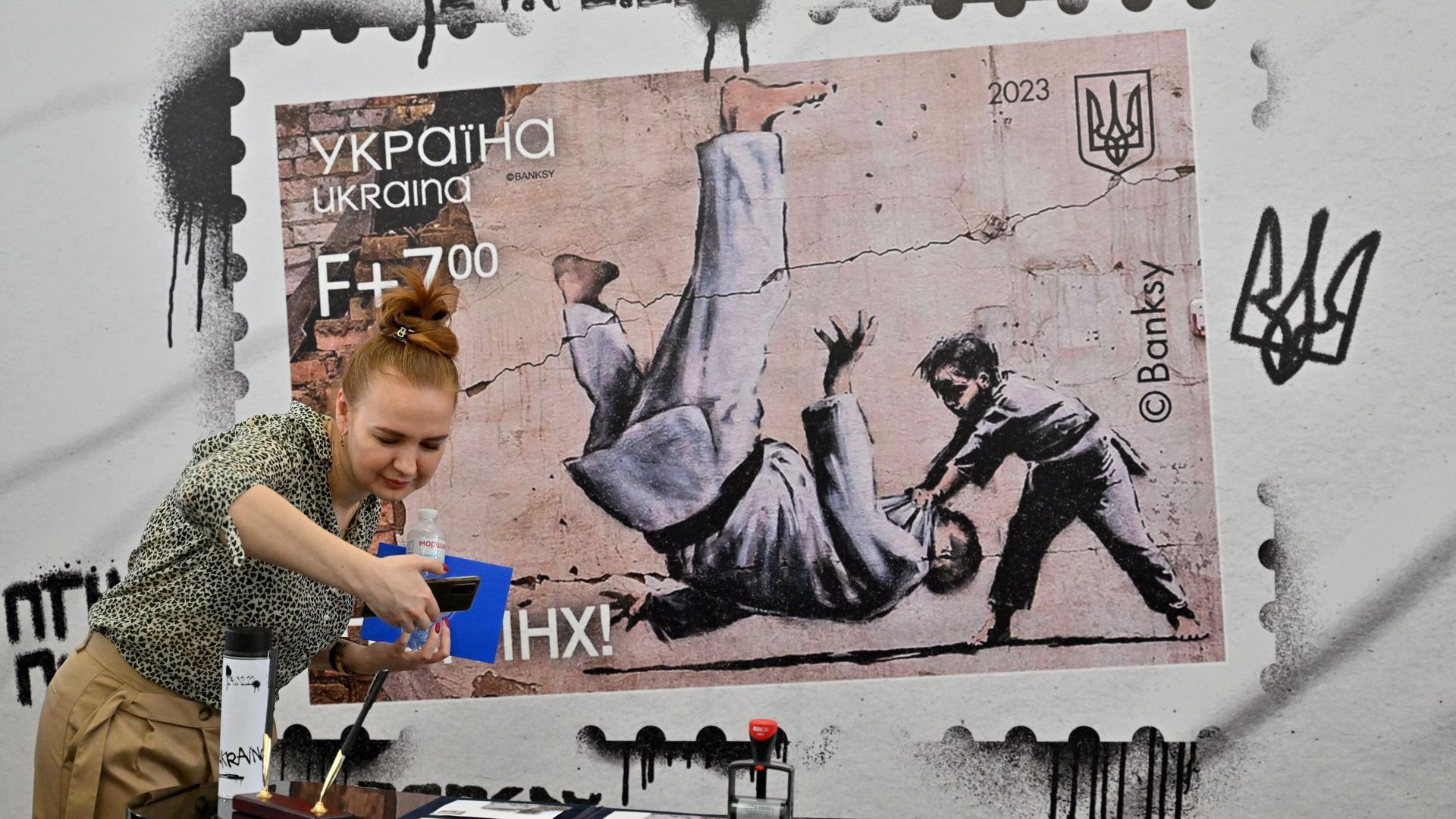 Une femme prend une photo de timbres et d’enveloppes au bureau de poste principal lors de la présentation d’un nouveau timbre ukrainien avec une image de Banksy, à Kiev le 24 février 2023.