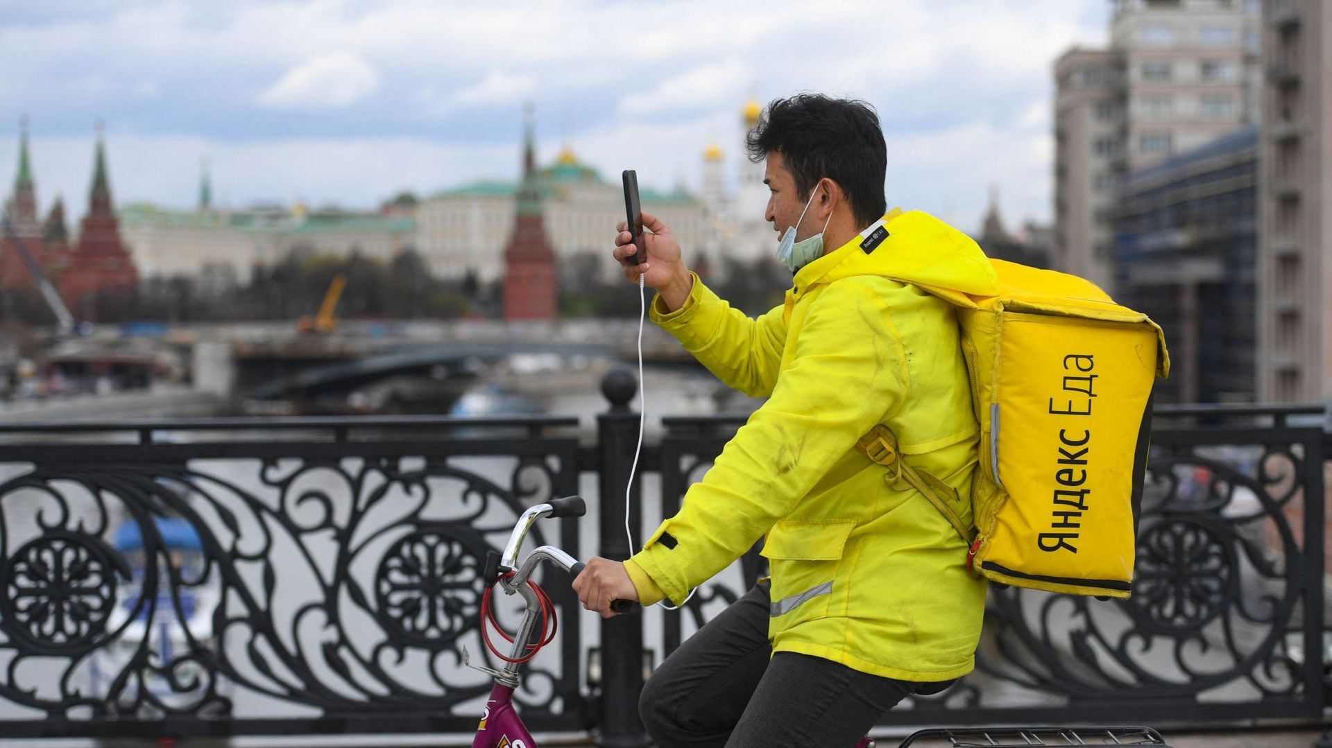 Un coursier de livraison de nourriture Yandex.Eats utilise son smartphone assis sur un vélo à un pont sur la rivière Moskva au centre-ville de Moscou.
