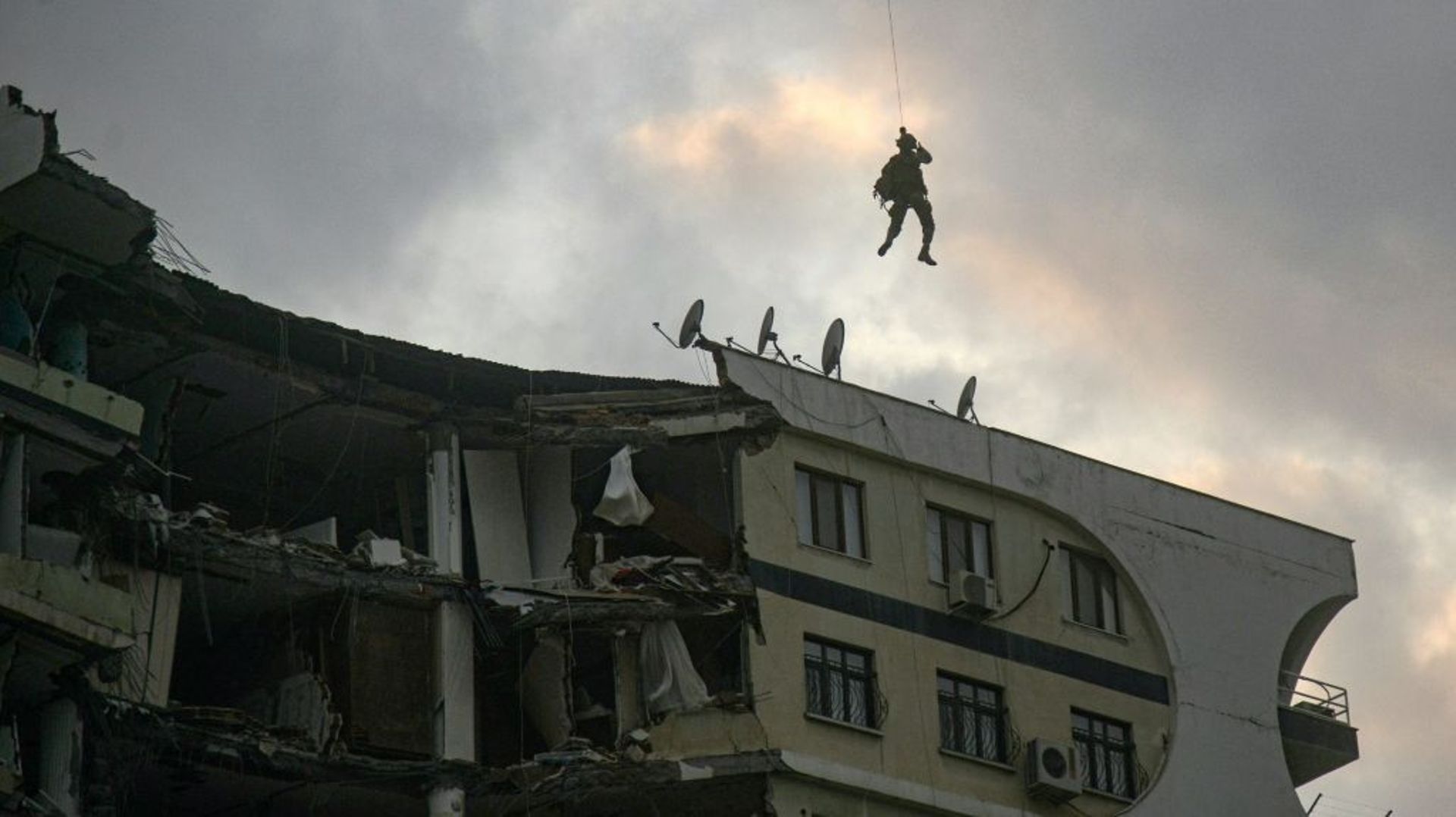 Un membre des forces spéciale, suspendu par un treuil à un hélicoptère, tente d'approcher le toit d'un immeuble endommagé pour secourir des animaux prisonniers des décombres, le 22 février 2023 à Diyarbakir, en Turquie