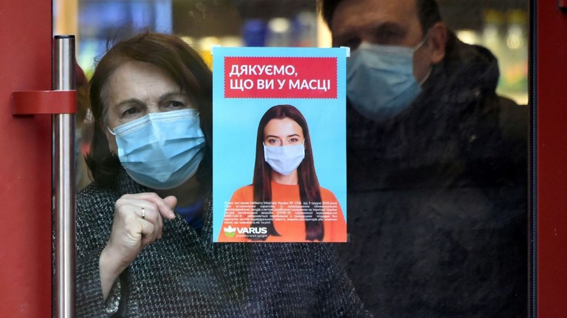Un couple devant une vitre sur laquelle une affiche incitant à porter le masque est collée, avant l’invasion russe, le 28 octobre 2021