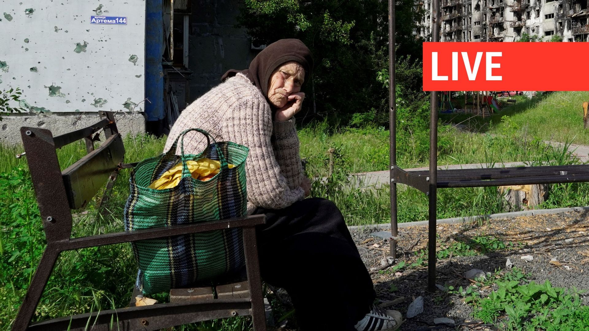 Une femme âgée est assise sur un banc dans une cour de bâtiments résidentiels détruits à Marioupol le 31 mai 2022.