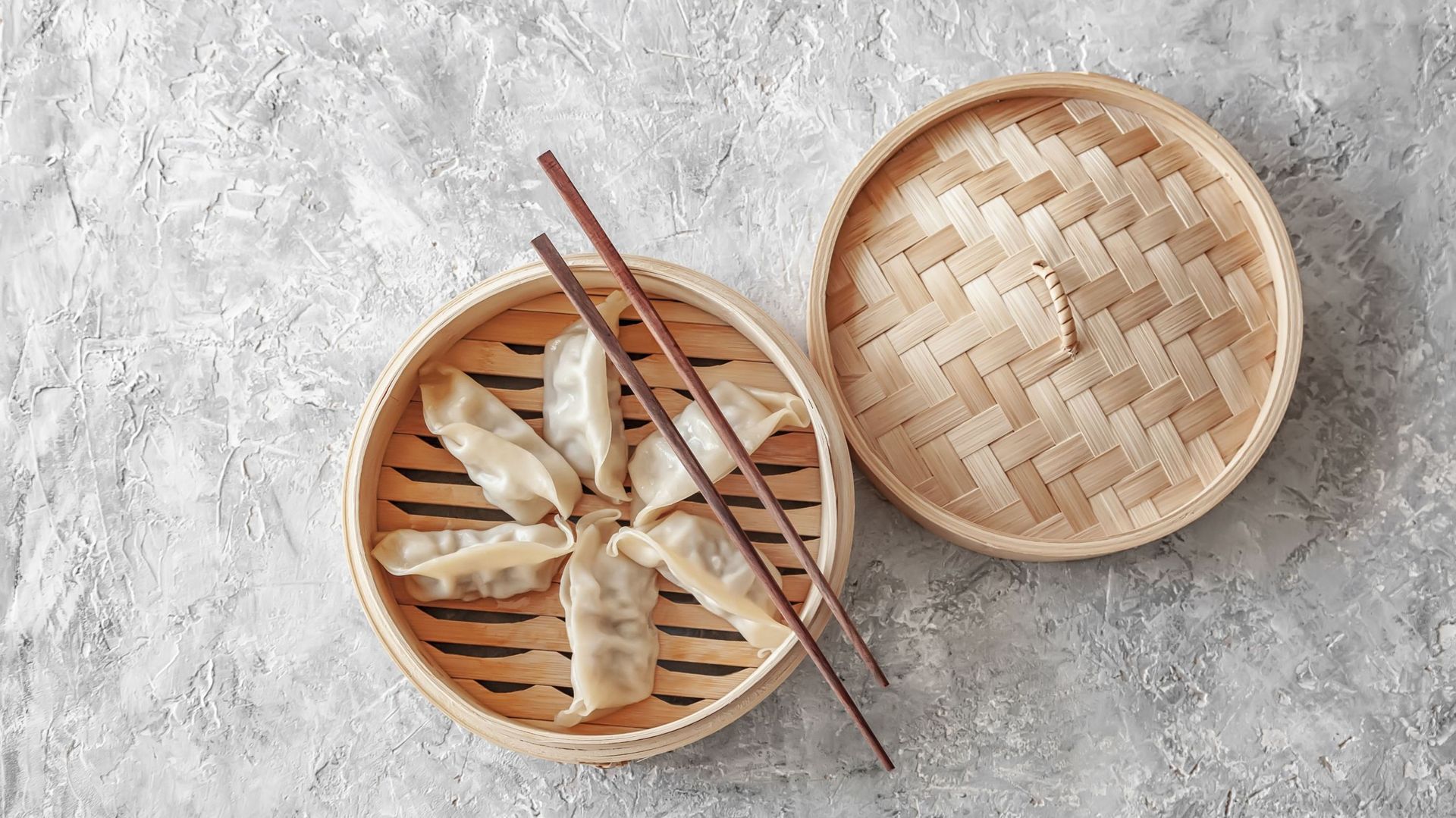 Steamed Chinese dumplings (Jiaozi) on bamboo steamer and chopsticks, concrete background, top view