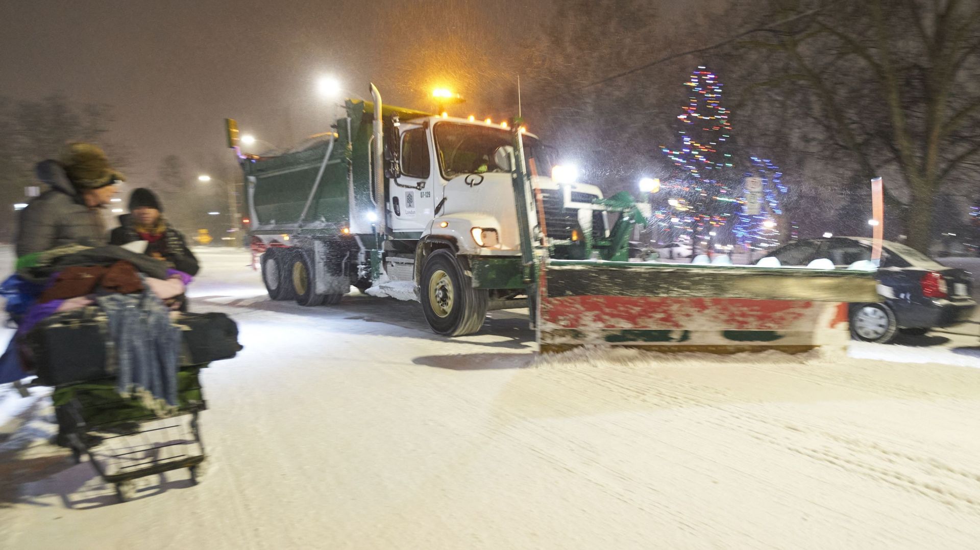 Un chasse-neige passe devant des piétons marchant dans la rue lors d’une grande tempête hivernale à London, Ontario, Canada, le 23 décembre 2022.