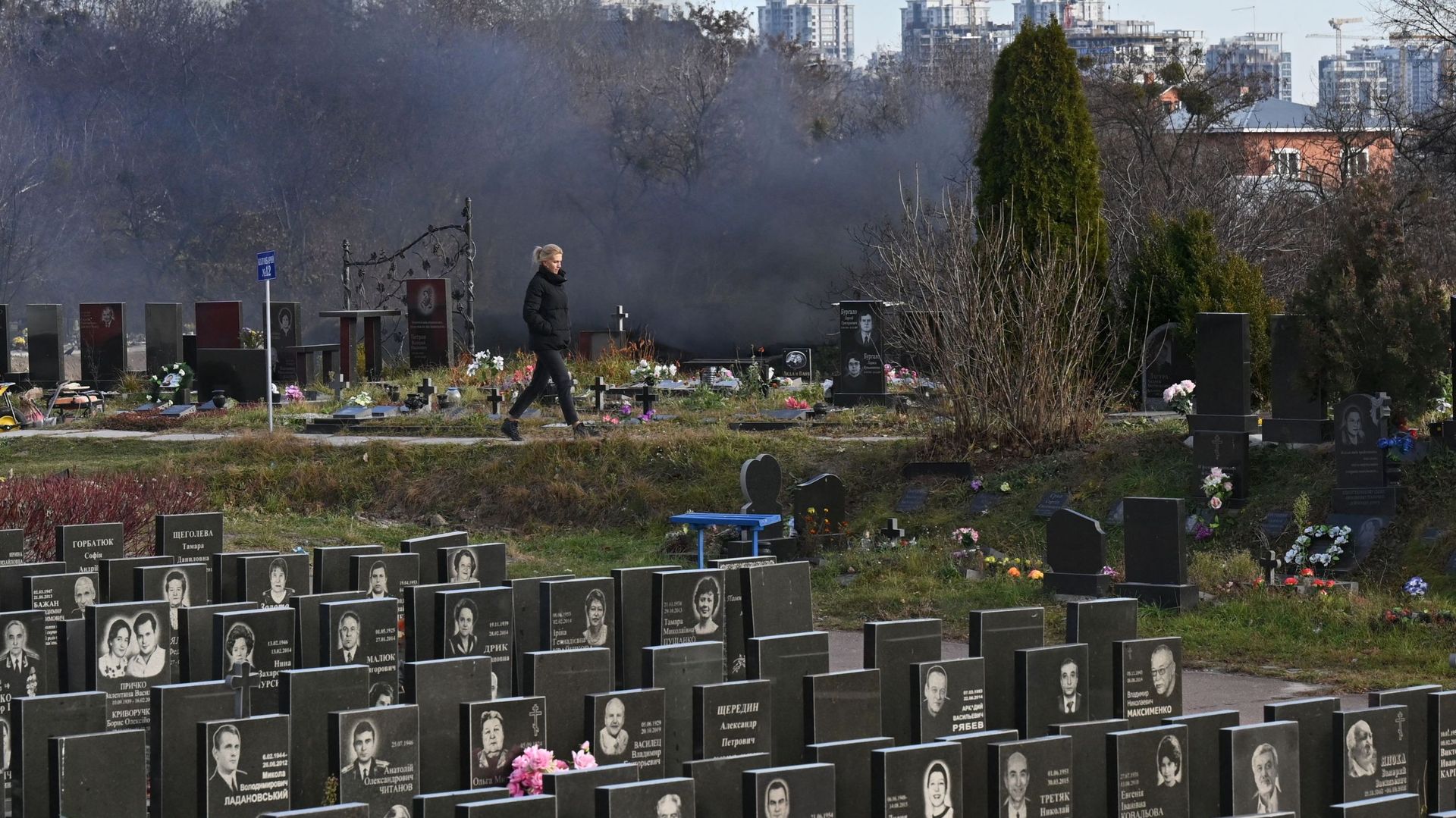 Une femme passe devant la cheminée fumante d'un crématorium dans un cimetière de Kiev, le 11 novembre 2021.