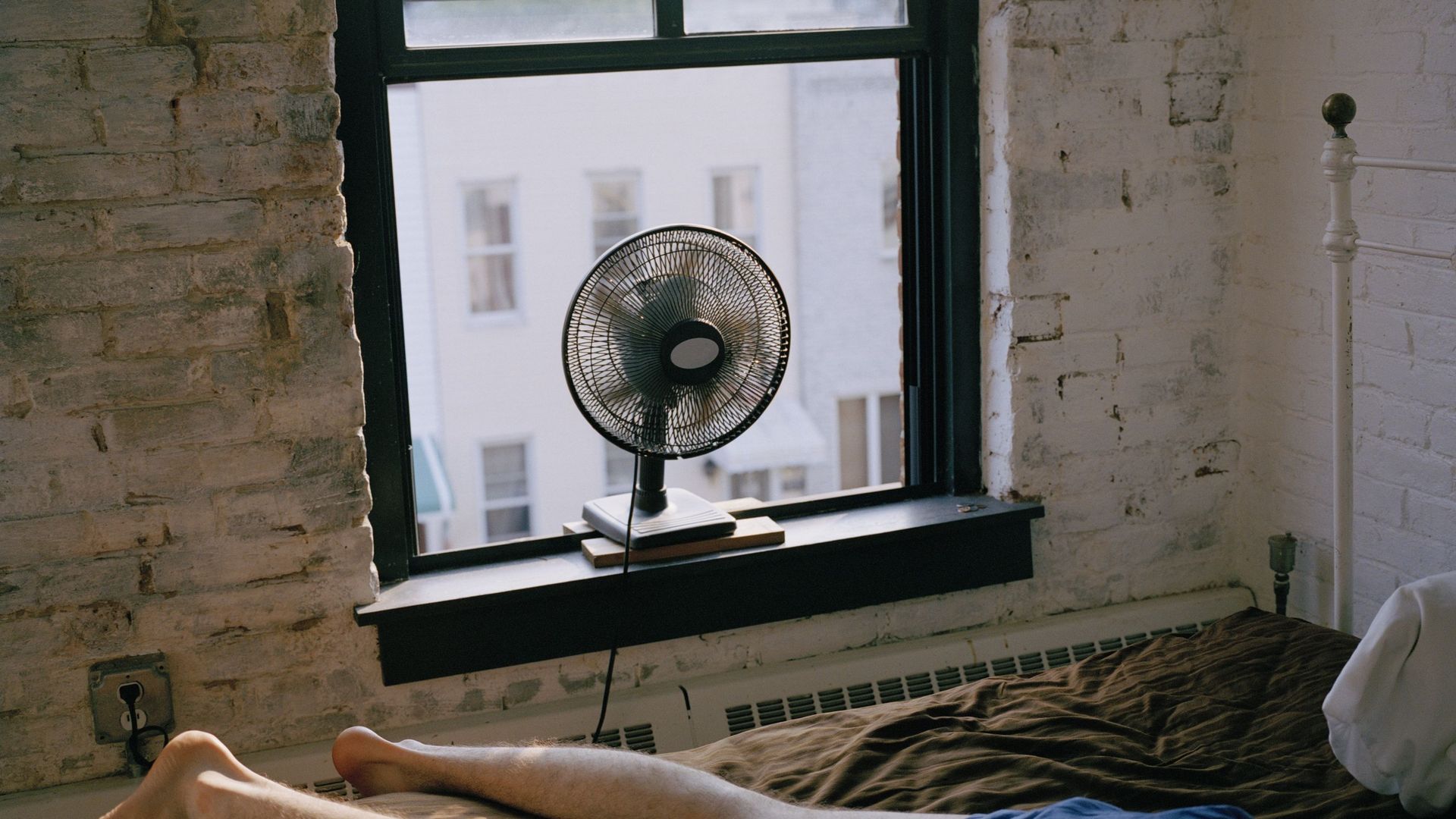 A man lying on a bed with a fan blowing