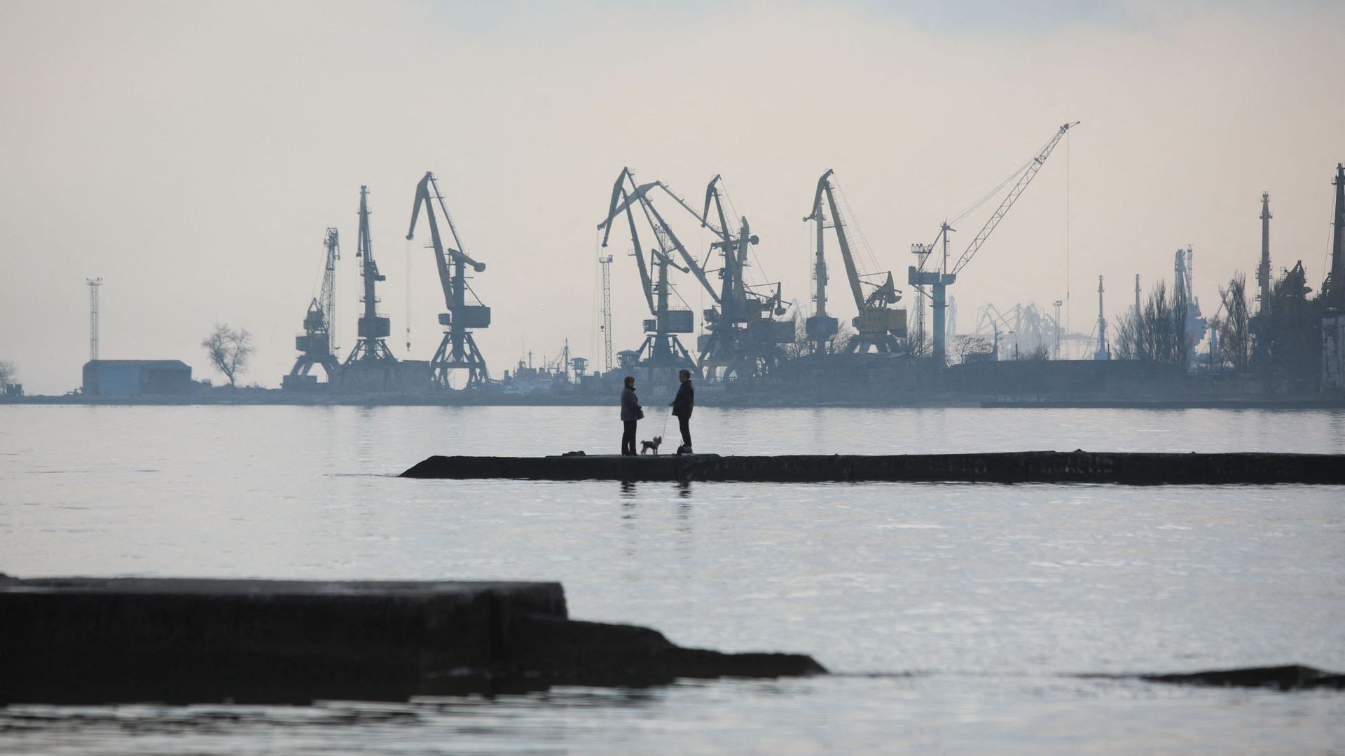 Un couple promène un chien sur une jetée au bord de la mer d'Azov, dans la ville portuaire industrielle de Mariupol, en Ukraine, le 23 février 2022.