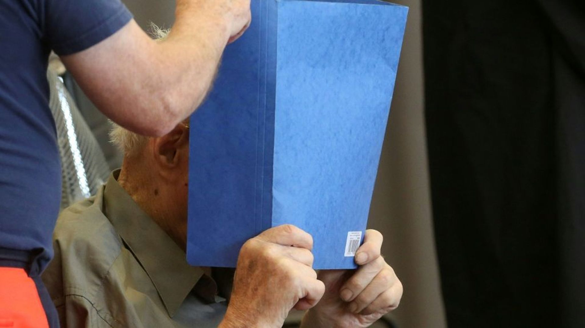 Josef Schütz, accusé de crimes nazis) cache son visage derrière un document à son arrivée au tribunal de Brandebourg-sur-la-Havel, le 28 juin 2022 en Allemagne