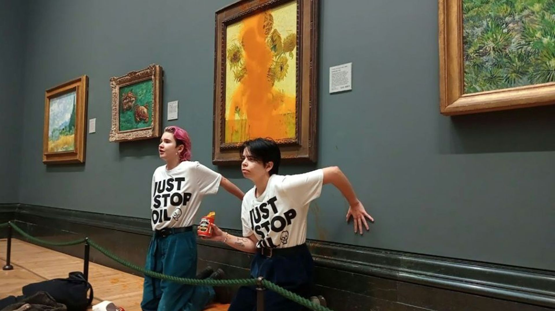 Photo diffusée par le groupe écologiste "Just Stop Oil" montrant des militantes, les mains collées au mur, devant le tableau les "Tournesols" du peintre Van Gogh aspergé de soupe à la tomate, le 14 octobre 2022 à la National Gallery de Londres