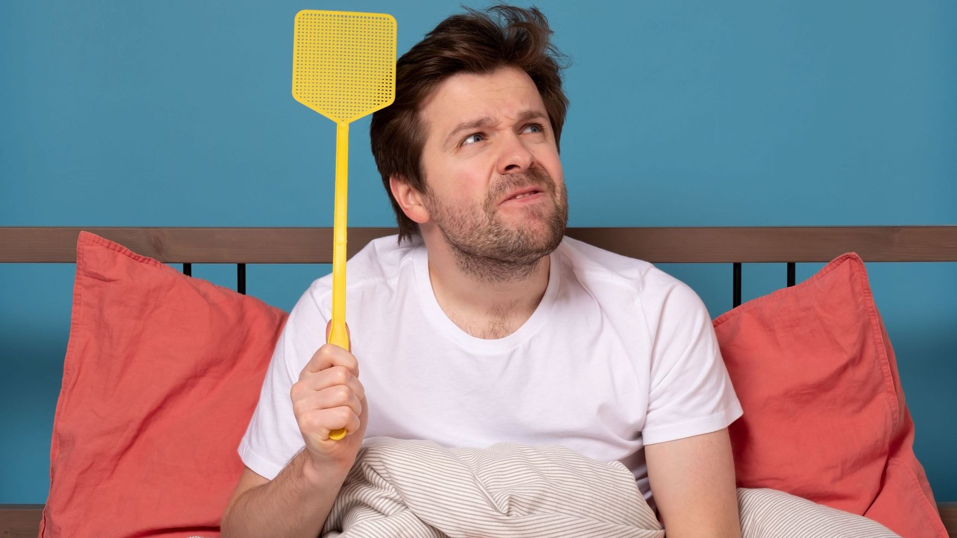 man holding a fly swatter wanting to kill annoying mosquito