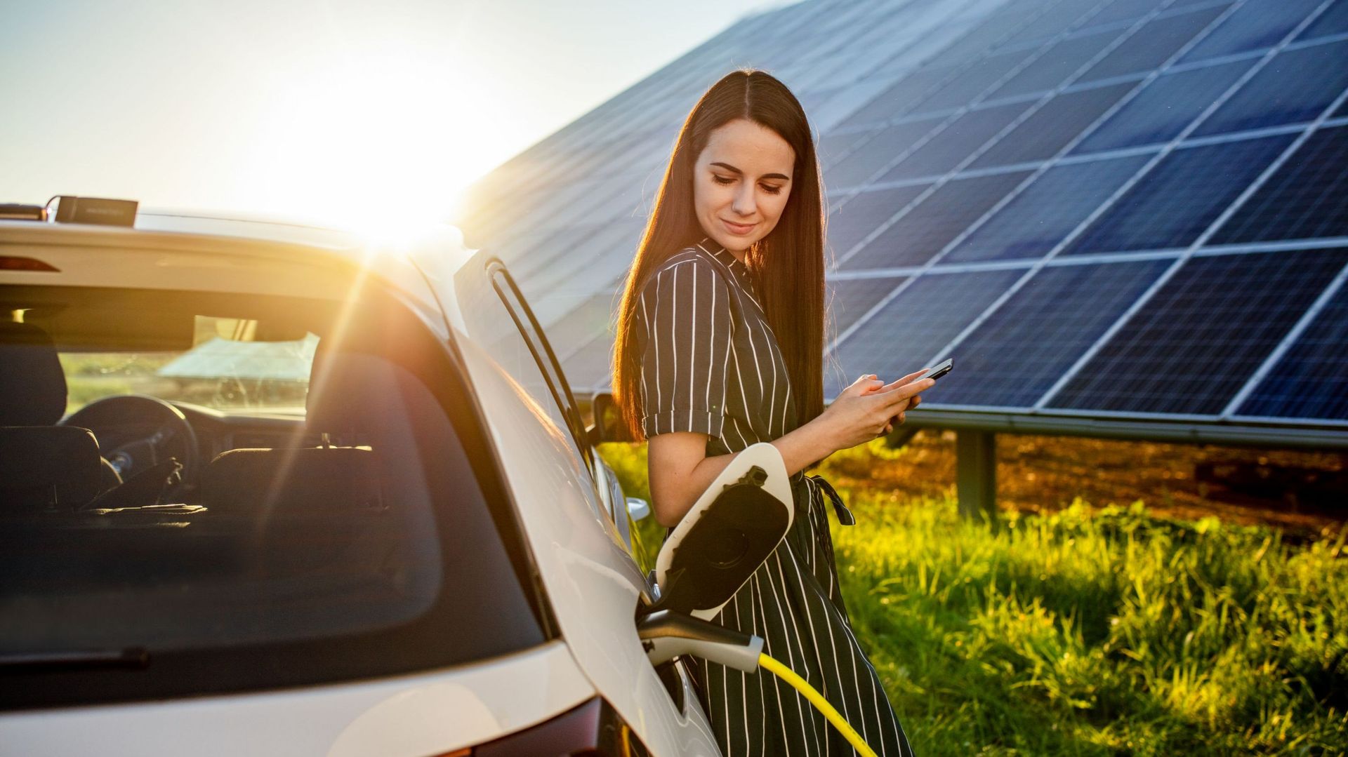 Femme attend la recharge de sa voiture électrique près de panneaux solaires