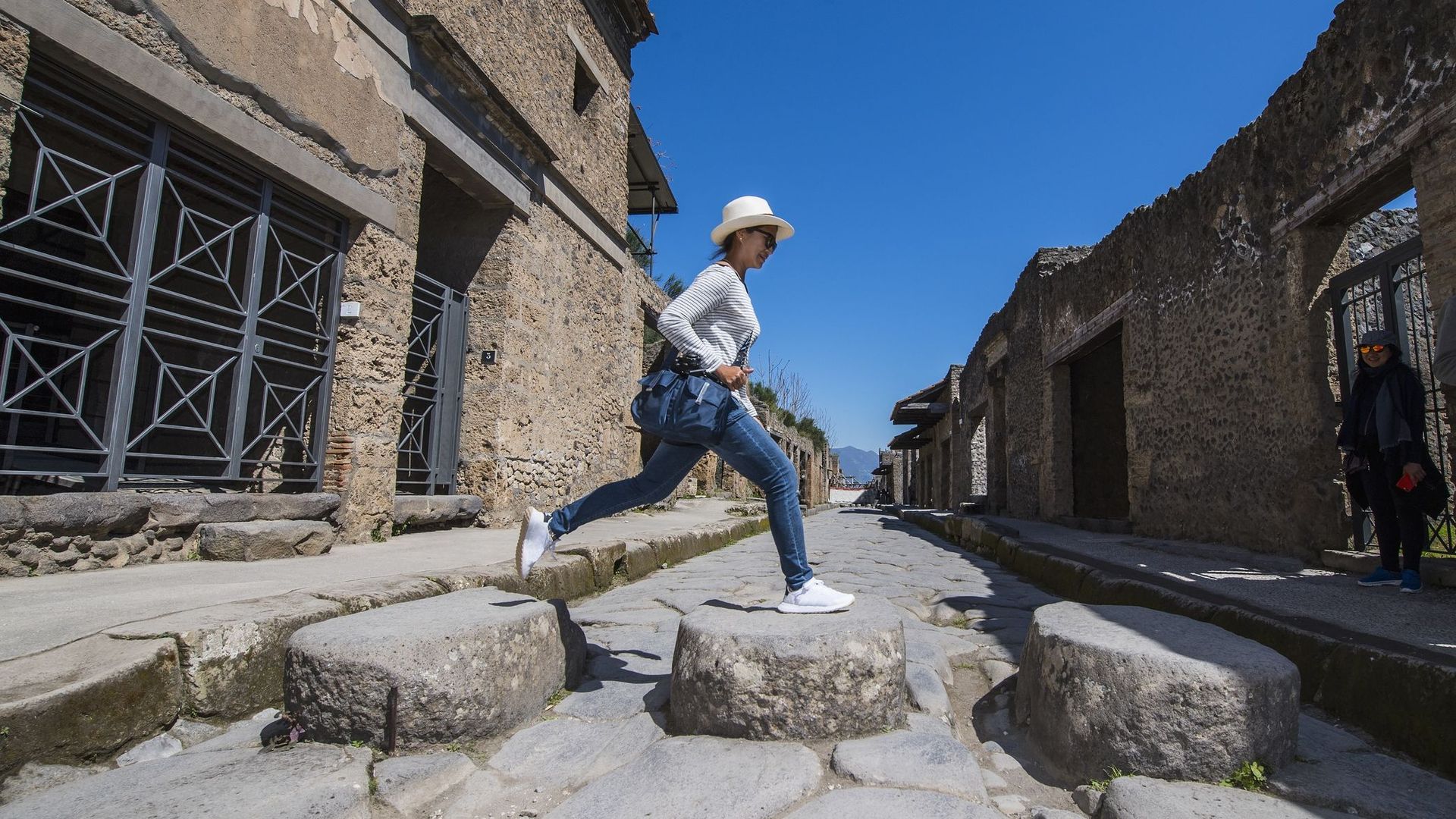 Female tourist jumping on stones in ruins of Pompeii, Naples, Italy