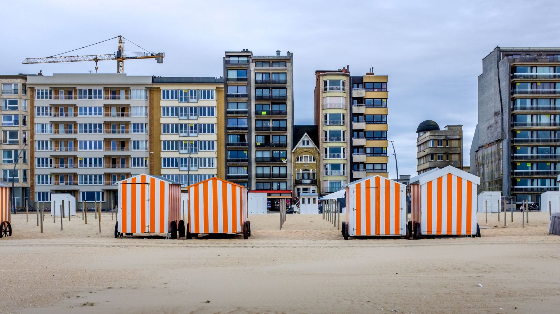 Row Of Colorful Beach Cabins Against Buildings In De Panne, Belgium