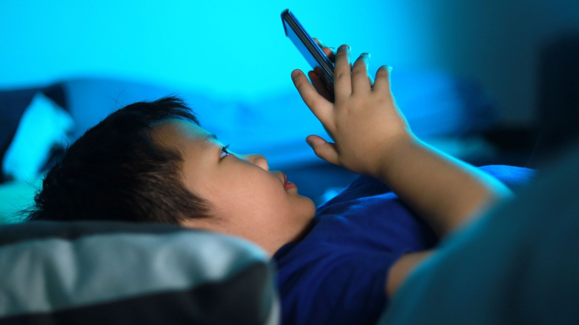 Garçon expose ses yeux à la lumière bleue de l’écran de son smartphone dans son lit.
