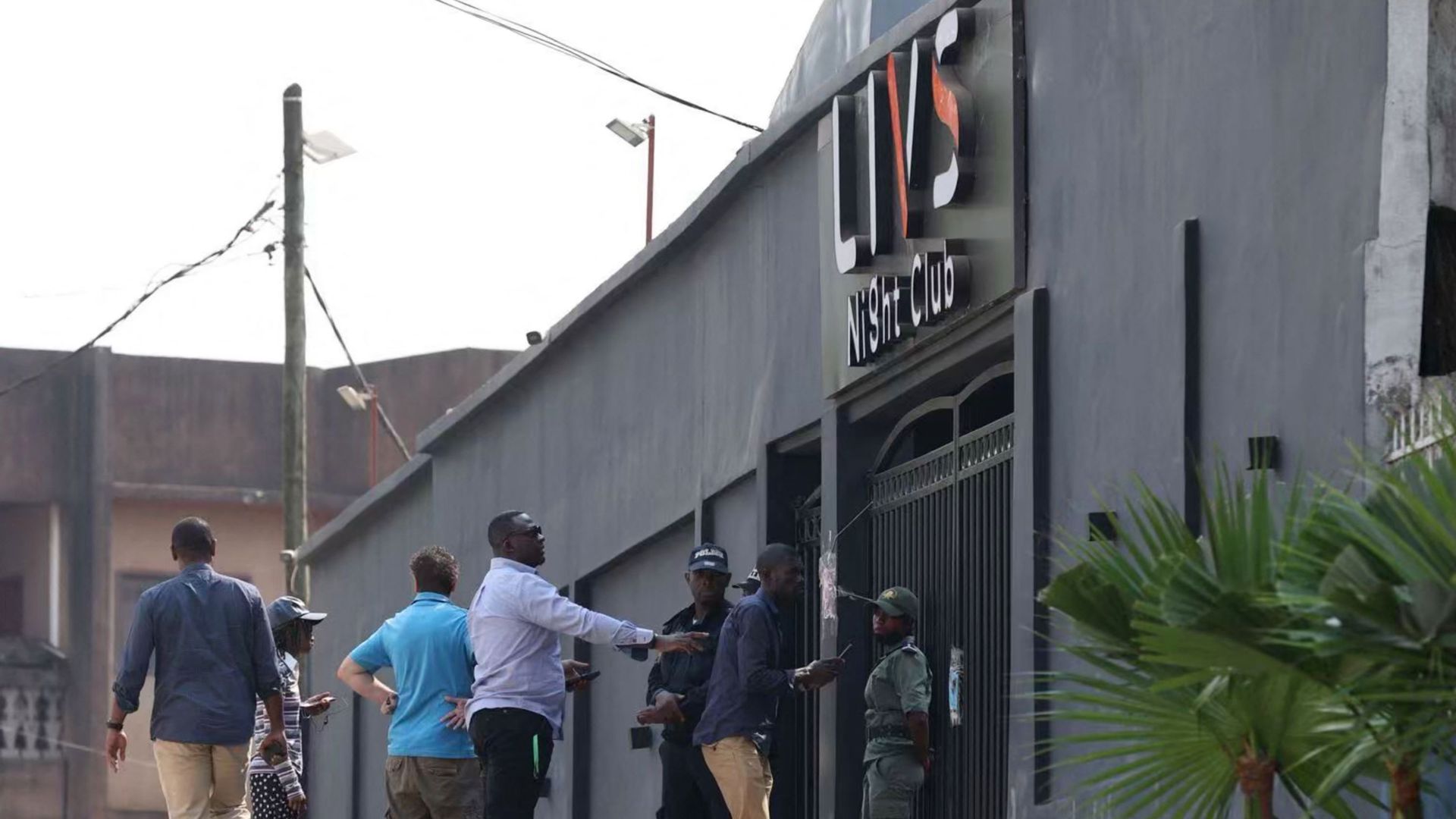 Des passants passent devant des policiers qui montent la garde à l'entrée de la discothèque Livs où un incendie meurtrier s'est déclaré dans le quartier Bastos à Yaoundé, le 23 janvier 2022. L'incendie accidentel, provoqué par un feu d'artifice, a fait au