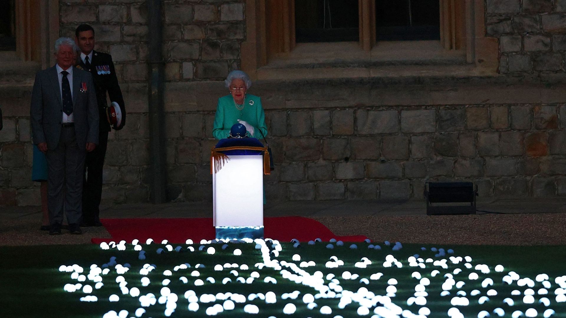 La reine Elizabeth II touche le globe des nations du Commonwealth pour lancer l'allumage du "Tree of Trees" au palais de Buckingham à Londres, depuis le château de Windsor, à l'ouest de Londres, le 2 juin 2022, dans le cadre des célébrations du jubilé de 