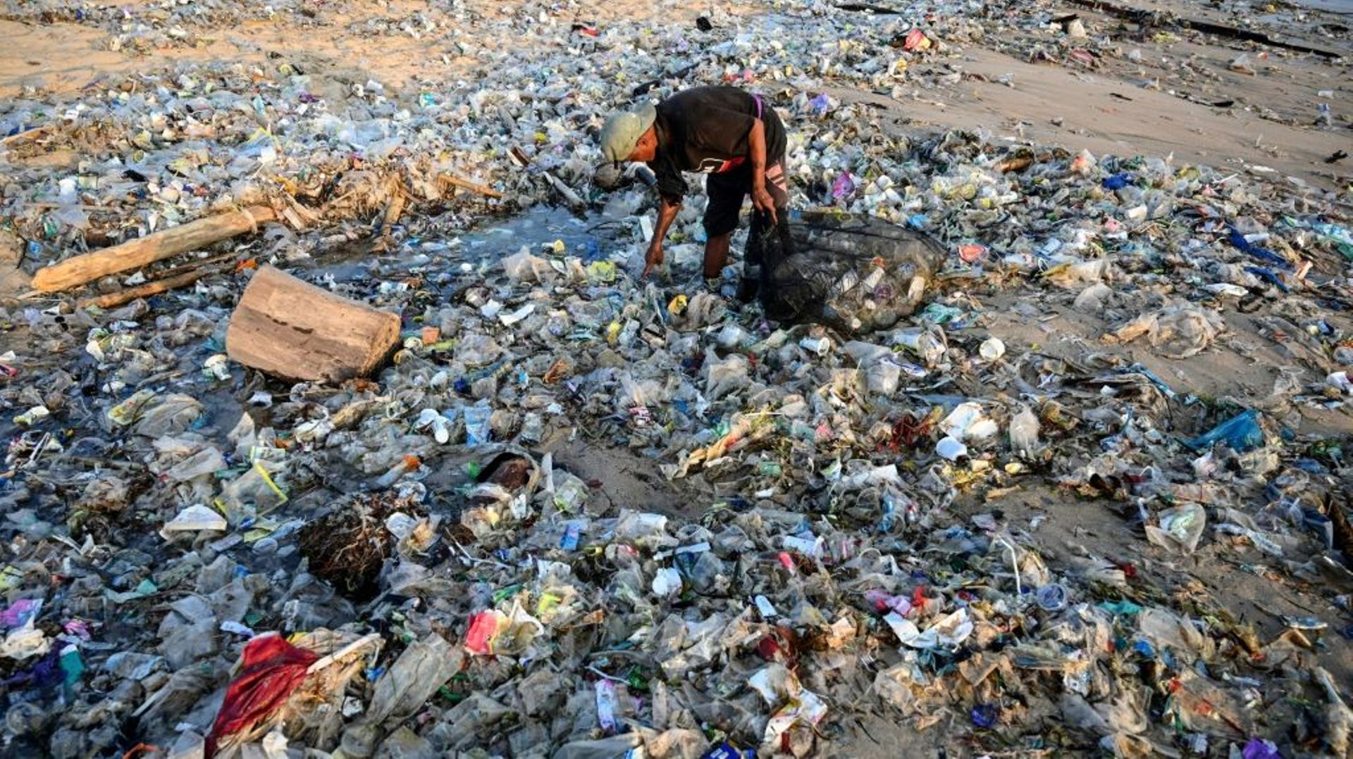 Un homme ramasse des déchets recyclables pour les revendre au milieu des ordures échouées sur la plage de Kedonganan, le 19 mars 2024 sur l’île indonésienne de Bali.