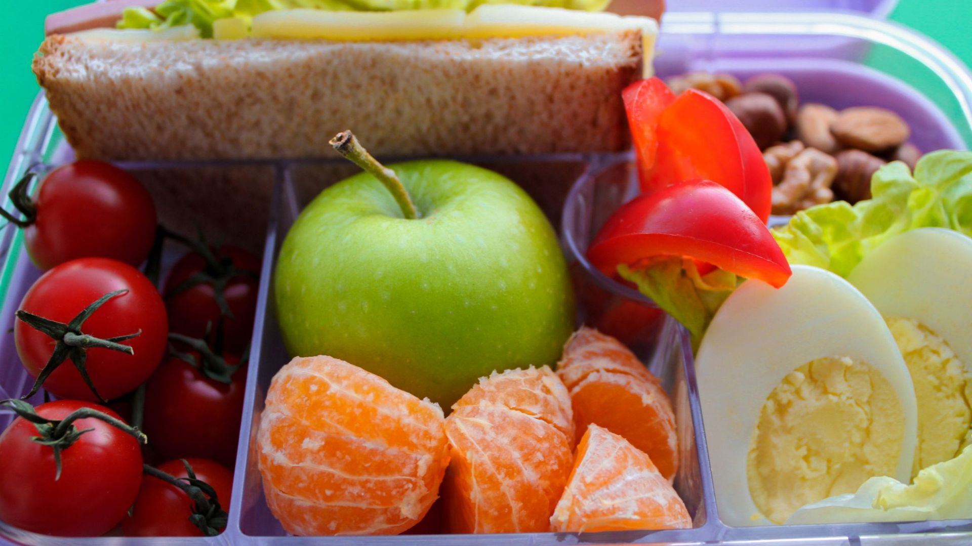 Close up of lilac lunch box with useful food for lunch and snack : sandwich, vegetables, fruits, nuts and eggs. Concept of healthy food, snack for adults and kids