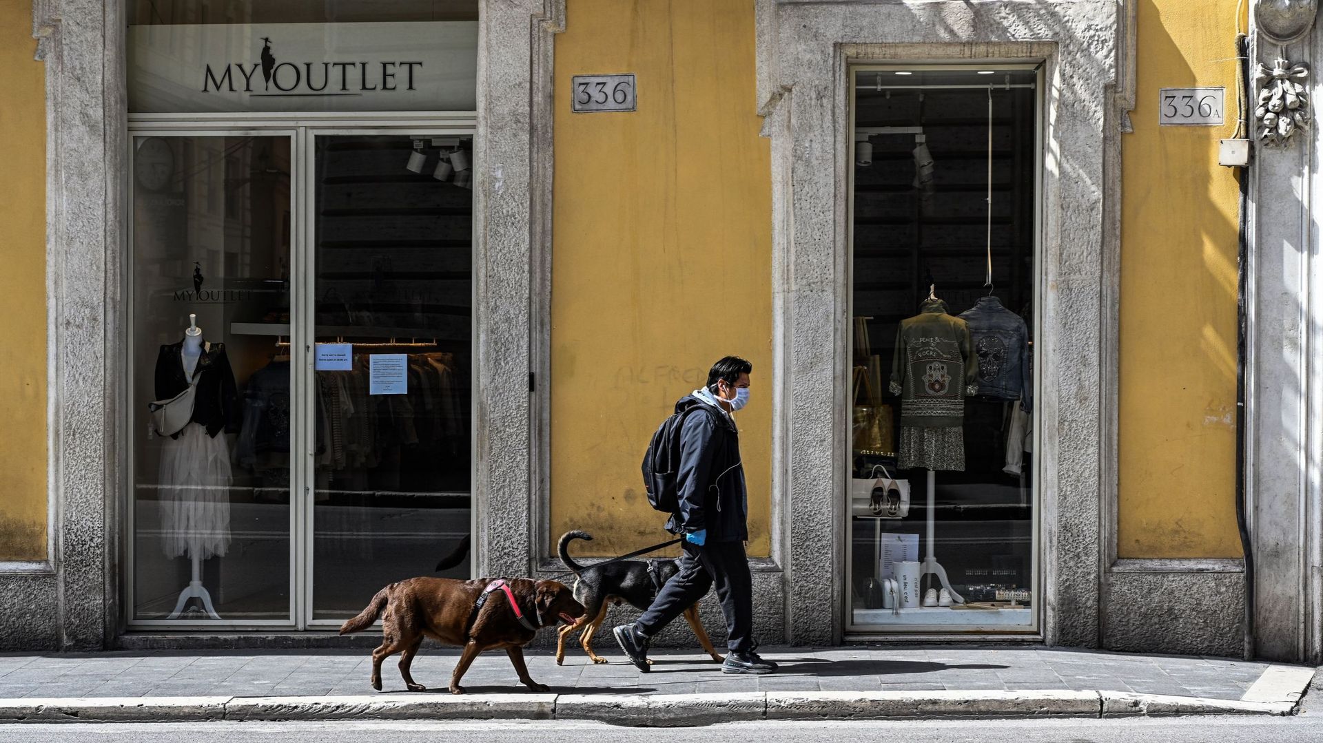 Un homme portant un masque facial promène ses chiens sur une principale rue commerçante déserte de la Via del Corso, le 31 mars 2020, dans le centre de Rome.