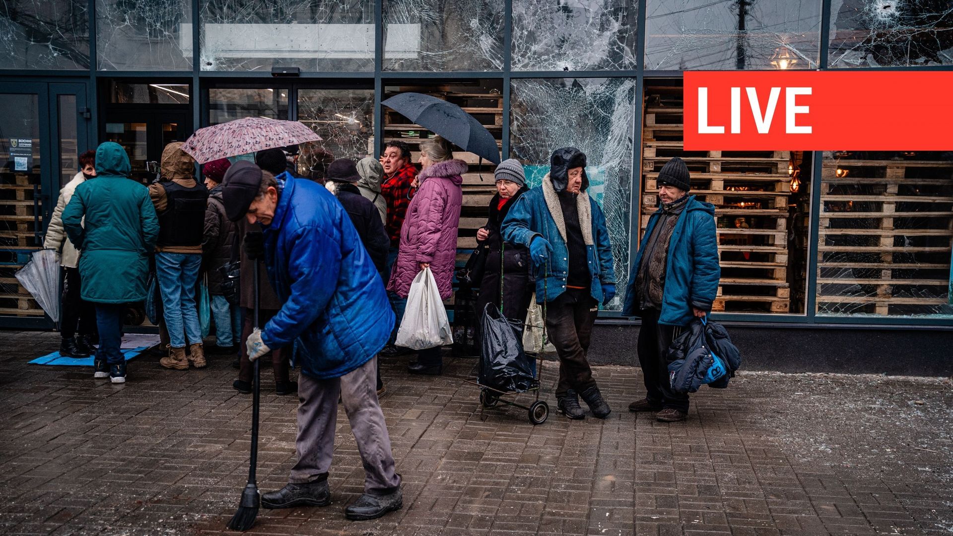 Des personnes font la queue devant un supermarché tandis qu'un homme nettoie après le bombardement de la ville ukrainienne de Kherson, le 25 décembre 2022.