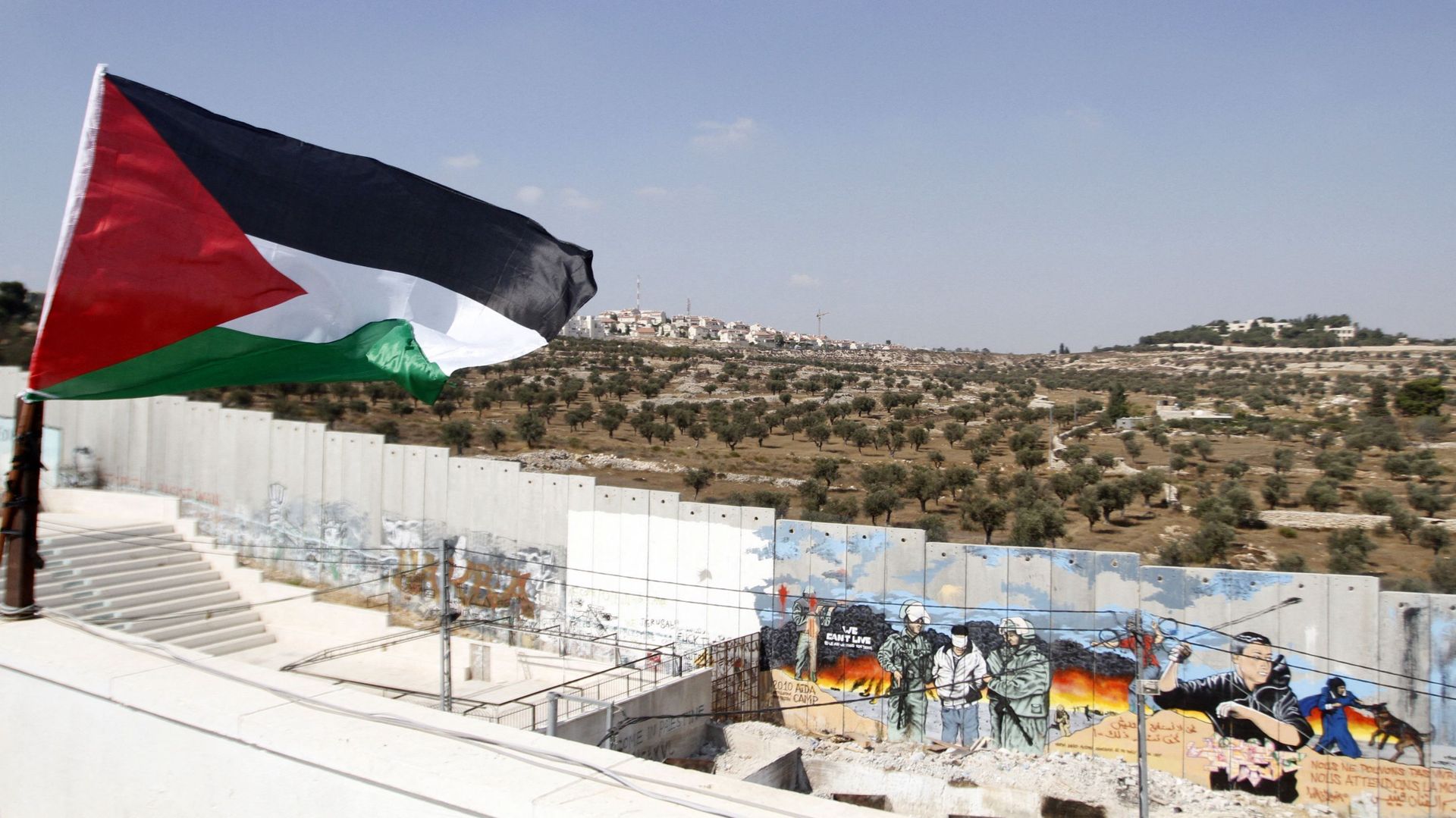 Un drapeau palestinien flotte à côté d’une section de la barrière de séparation controversée d’Israël dans le camp de réfugiés d’Aïda, près de la ville de Bethléem, en Cisjordanie.