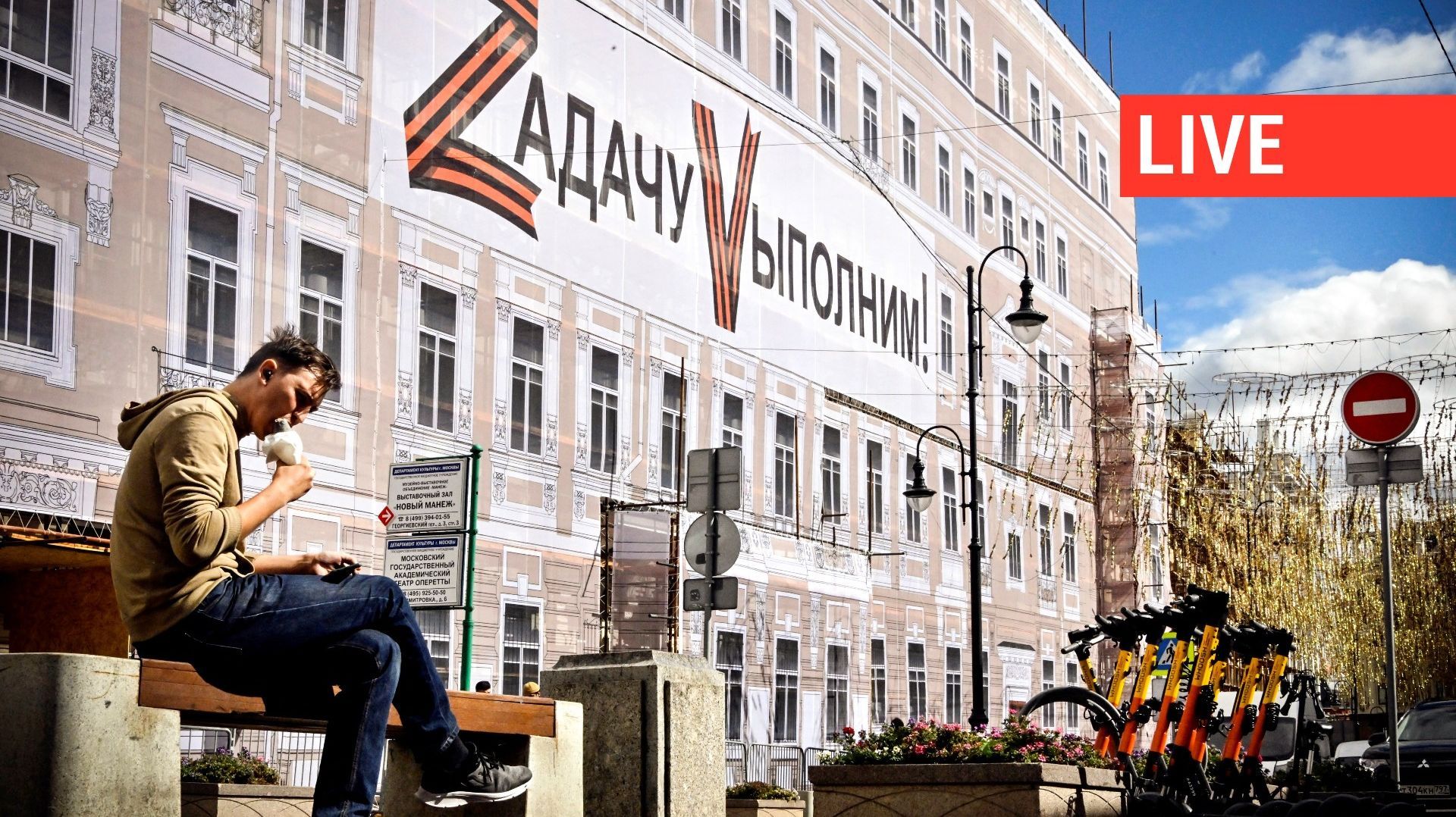Un homme est assis à côté d'une bannière montrant les lettres Z et V, insignes tactiques des troupes russes en Ukraine, et portant la mention "Nous accomplirons la tâche", sur le bâtiment administratif du théâtre Bolchoï, dans le centre de Moscou, le 2 se