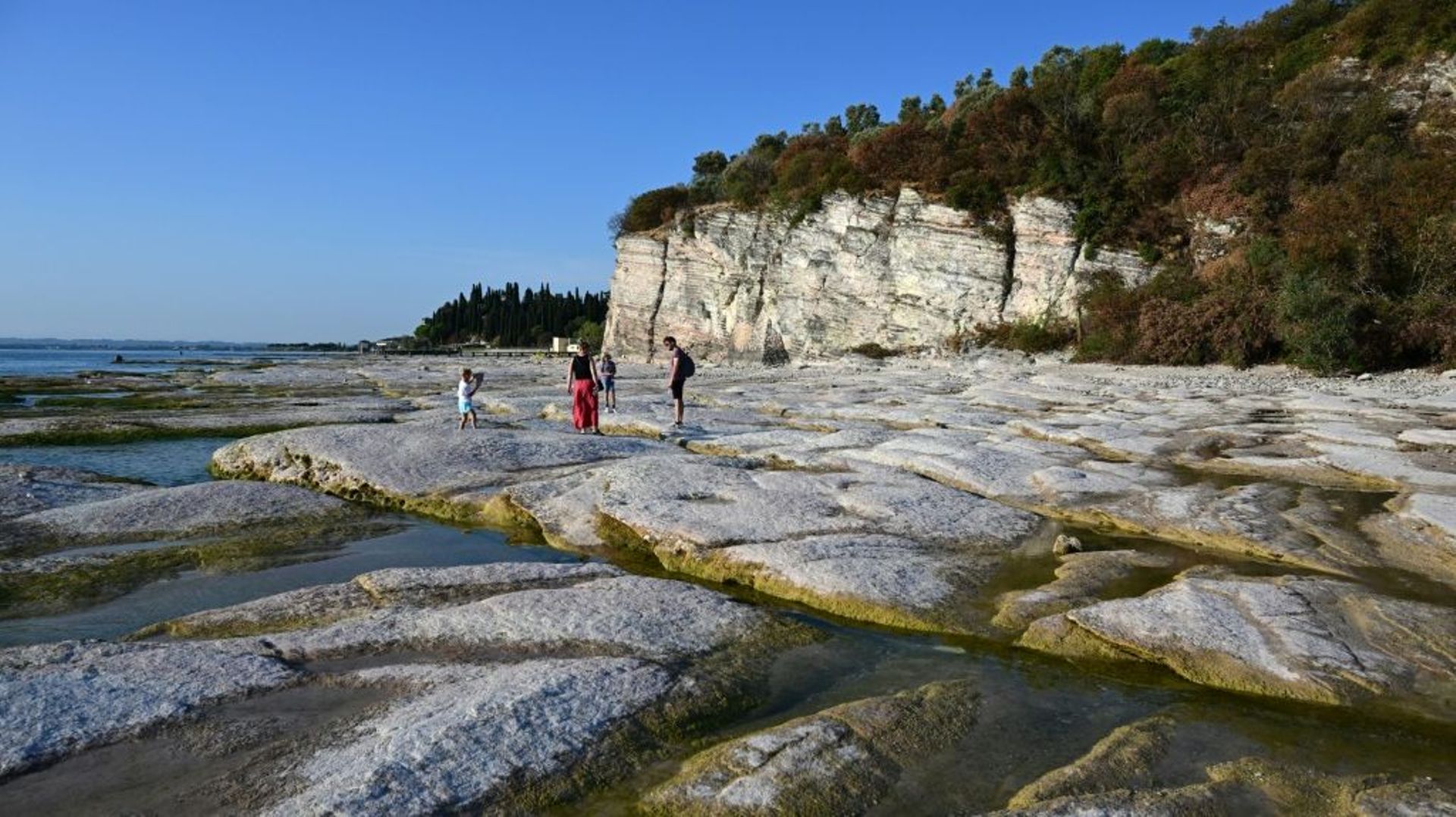 Des gens marchent le 16 août 2022 sur les rochers de la péninsule de Sirmione sur le lac de Garde en Italie
