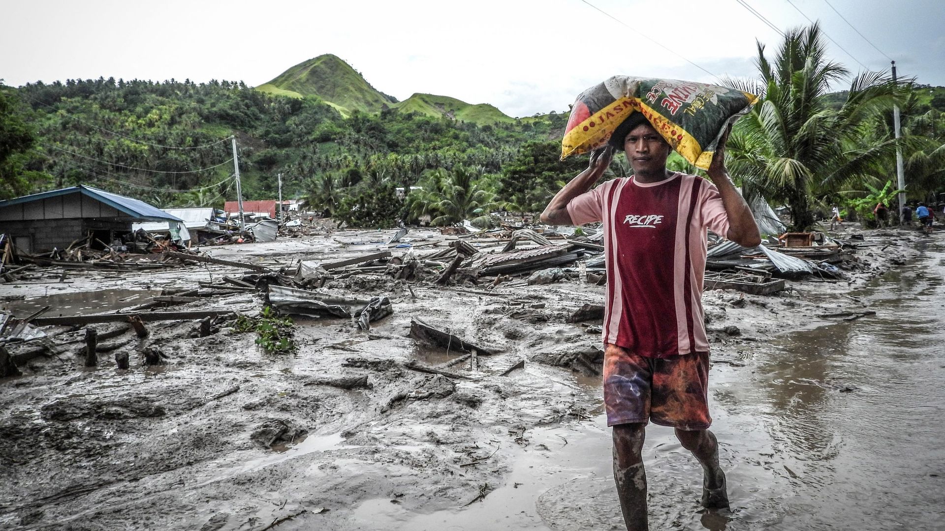Un habitant portant un sac de riz marche sur une route boueuse près d'une maison détruite dans le village de Kusiong, touché par un glissement de terrain à Datu Odin Sinsuat, dans la province de Maguindanao, dans le sud des Philippines, le 29 octobre 2022