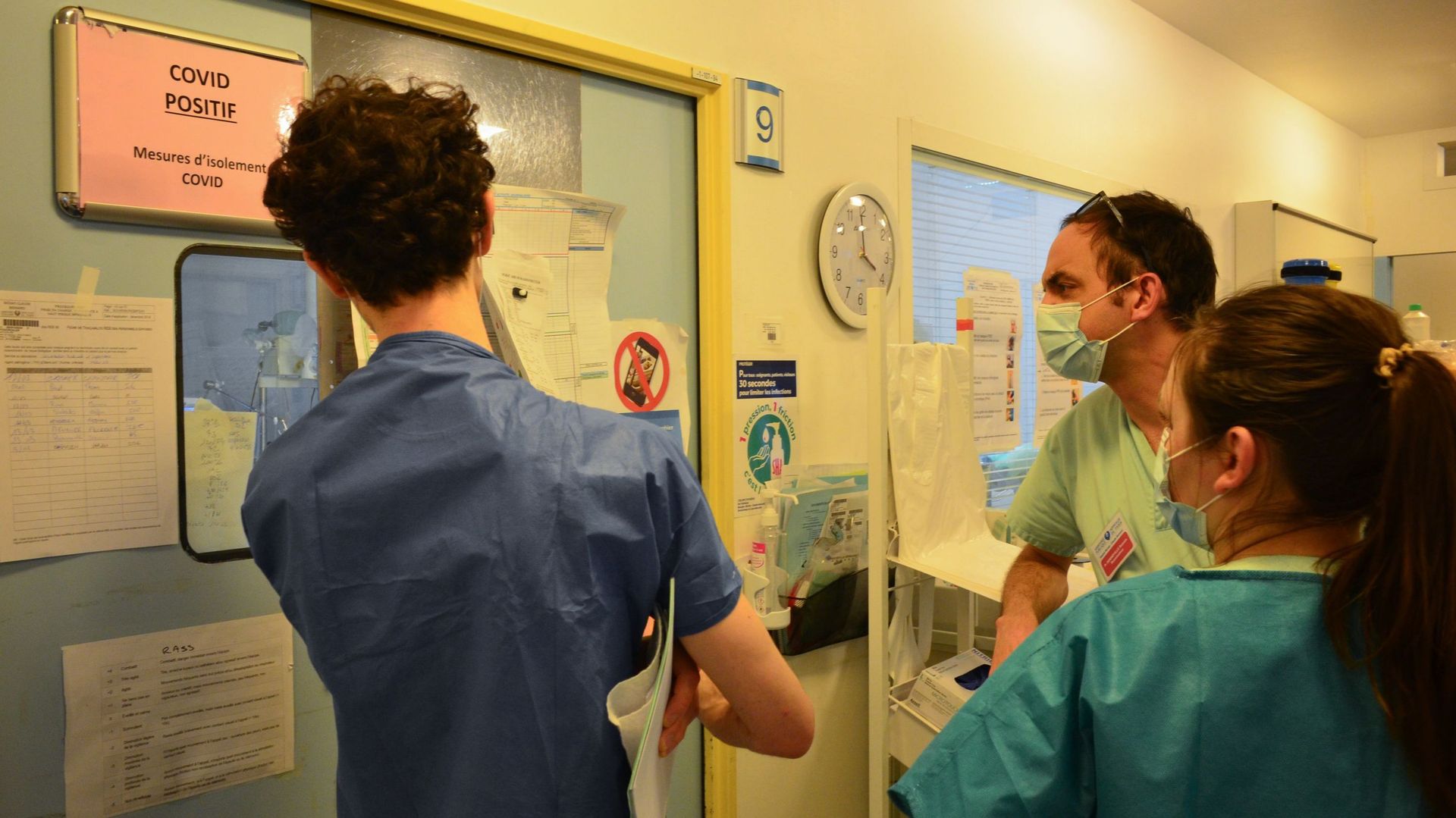 Un médecin s’entretient avec des membres du personnel alors qu’ils observent un patient atteint du nouveau coronavirus COVID-19 à travers une fenêtre de l’unité de soins intensifs de l’hôpital Bichat à Paris – 13 mars 2020.