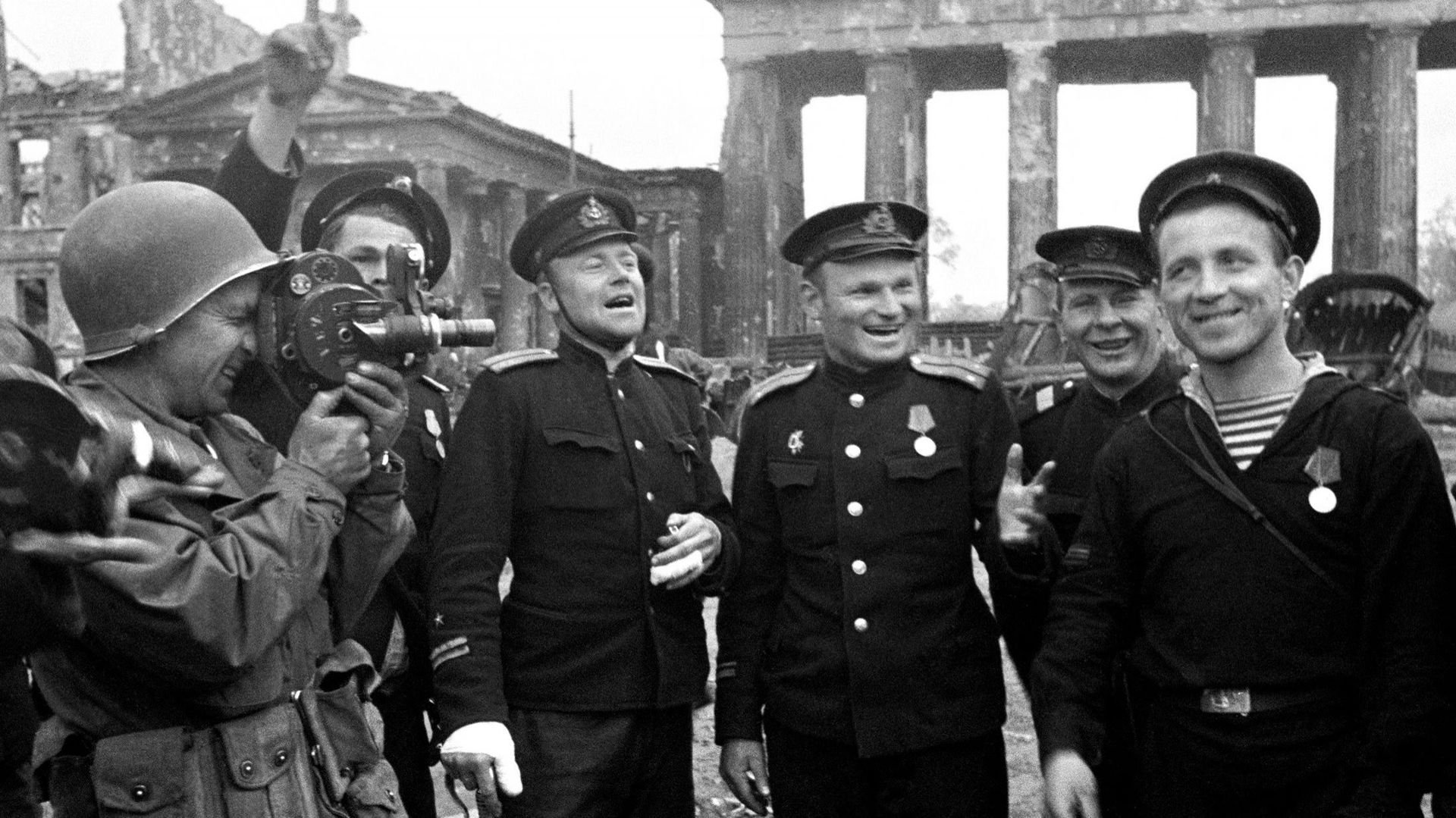 Des soldats soviétiques posent devant la porte de Brandebourg à Berlin, sous l’œil d’un caméraman américain, en mai 1945, au moment de la fin de la guerre.