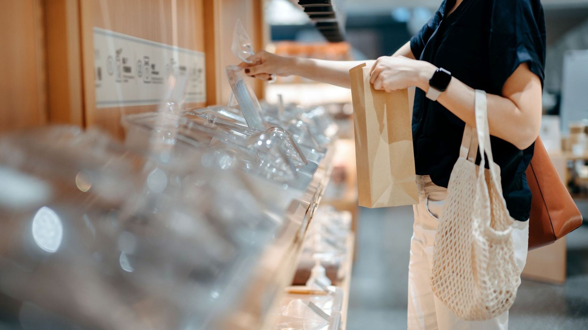 Young Asian woman carrying reusable cotton mesh bag doing grocery shopping, holding a paper bag and self-serving in a package-free organic whole foods refill store. Zero waste, plastic free, ecologically friendly, green living and sustainable lifestyle