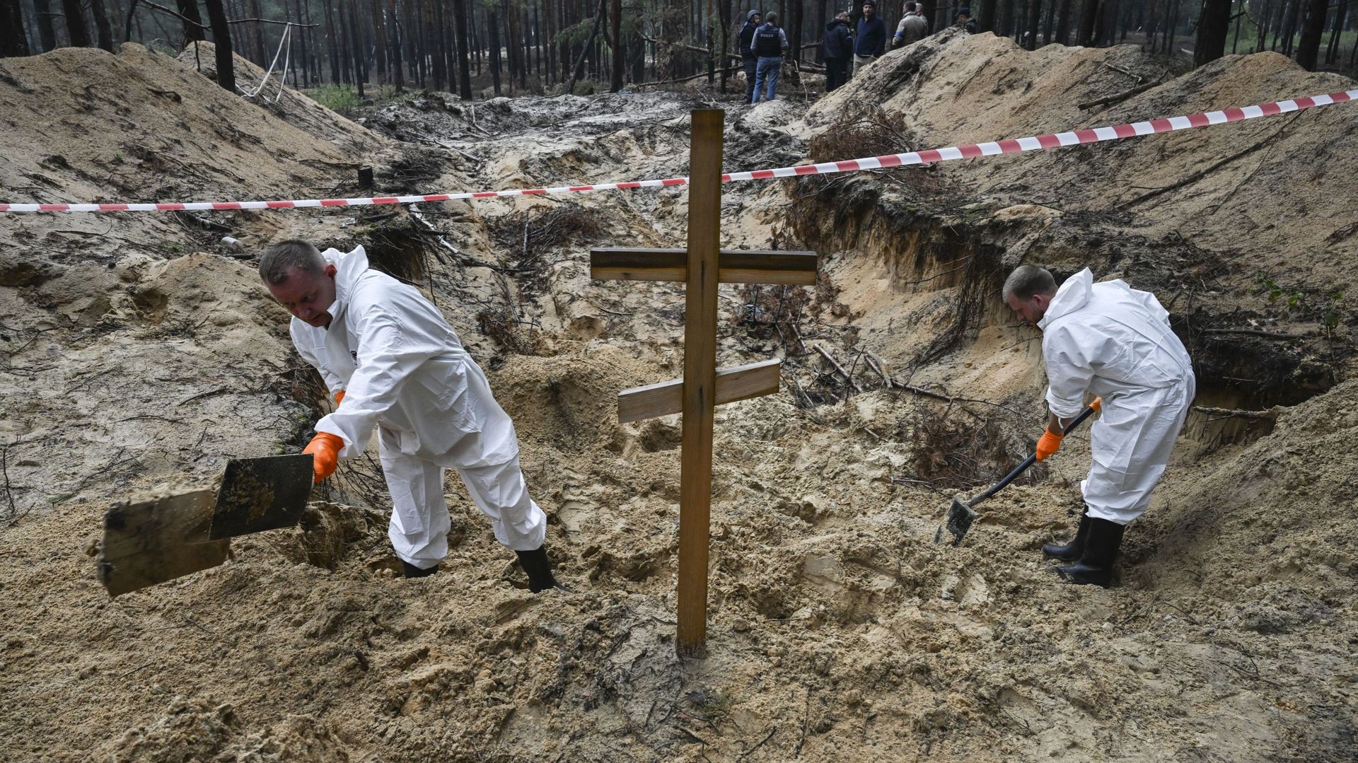 Deux techniciens médico-légaux creusent près d’une croix dans une forêt à la périphérie d’Izyum, dans l’est de l’Ukraine, le 16 septembre 2022. L’Ukraine a déclaré le 16 septembre 2022 avoir recensé 450 tombes sur un seul site funéraire près d’Izyum après