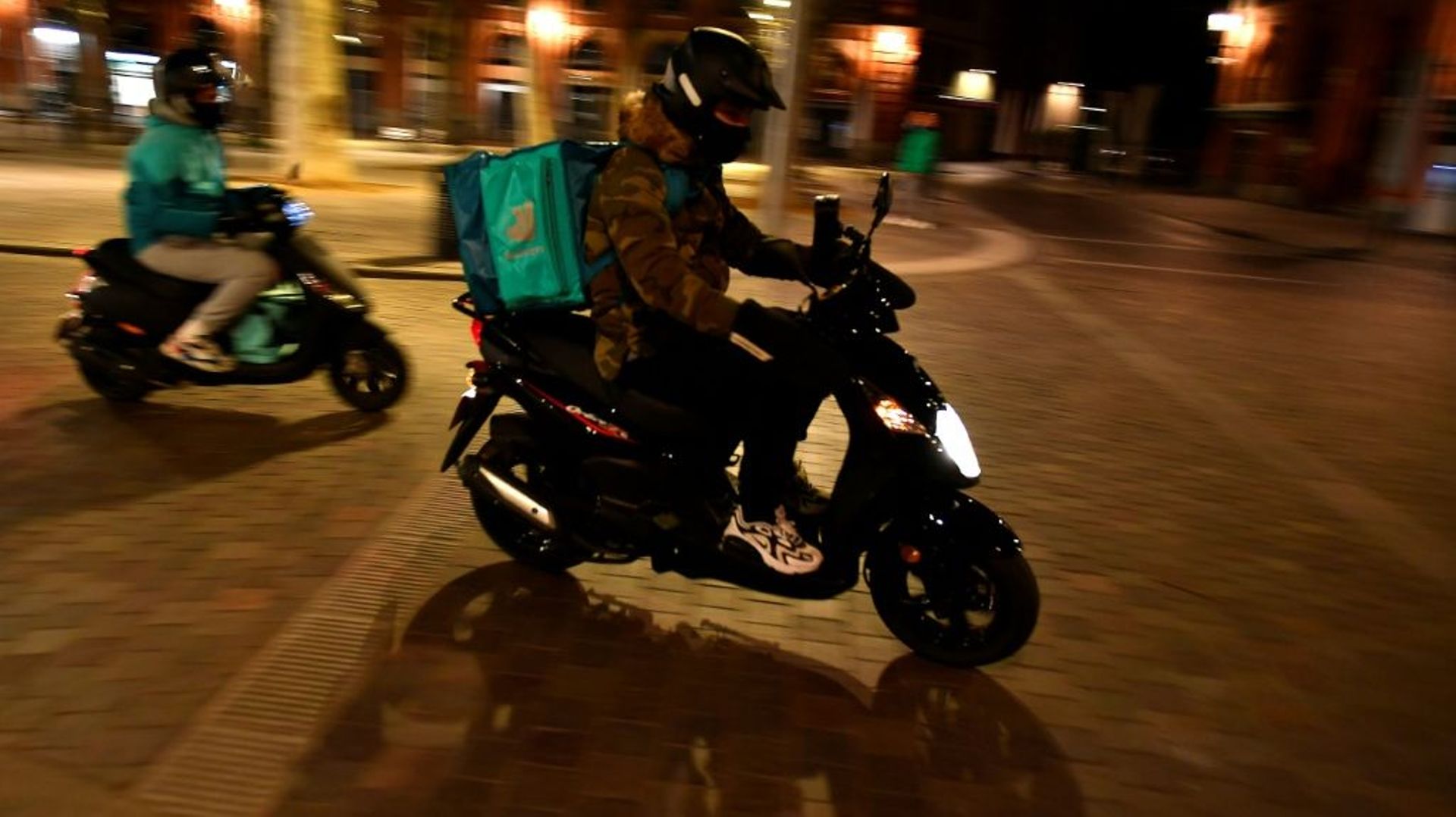 Deux liveurs à scooter Deliveroo traversent la Place Saint Pierre à Toulouse, le 16 janvier 2021