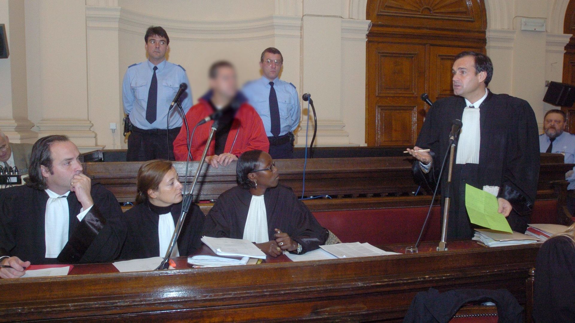 Lors du procès de 2005 aux Assises de Mons, un seul accusé présent derrière ses trois avocats. La chaise de Nicolas Theodorou est vide.  Sur le cliché, on aperçoit Maître Mayence (à droite) lire la lettre de son client dans laquelle Nicolas Théodorou disa