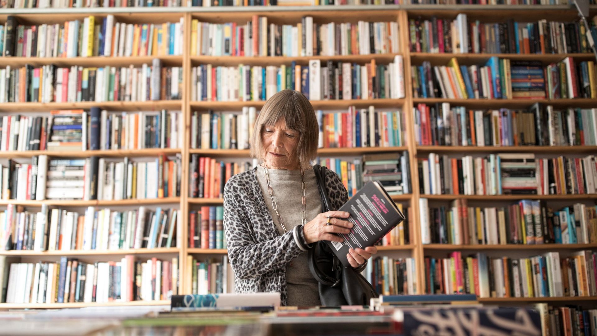 Senior woman with book standing against bookshelf