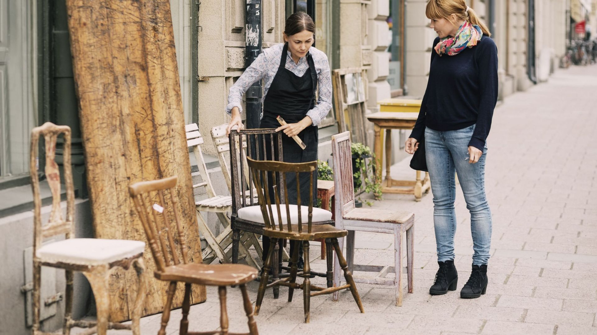 Female retailer showing antique chair to customer outside antique shop