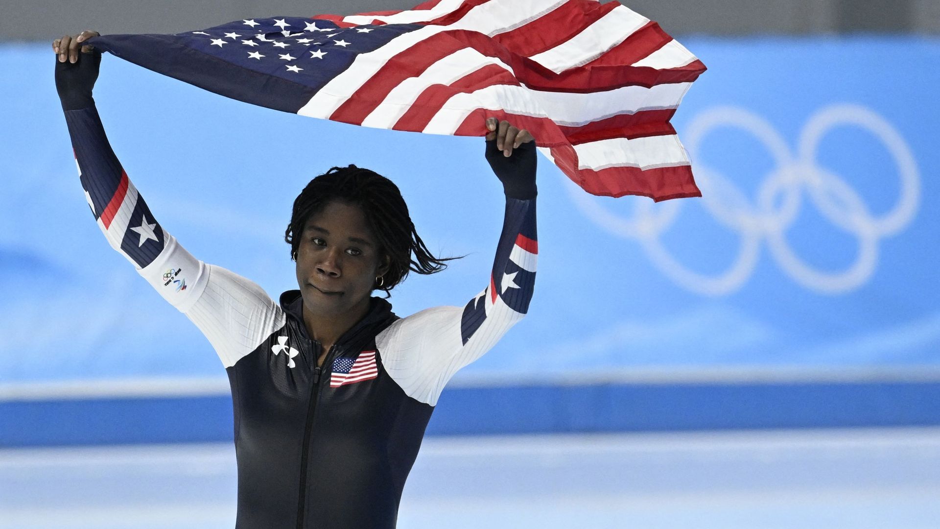 Erin Jackson célèbre sa victoire, faisant flotter le drapeau américain au-dessus de sa tête.