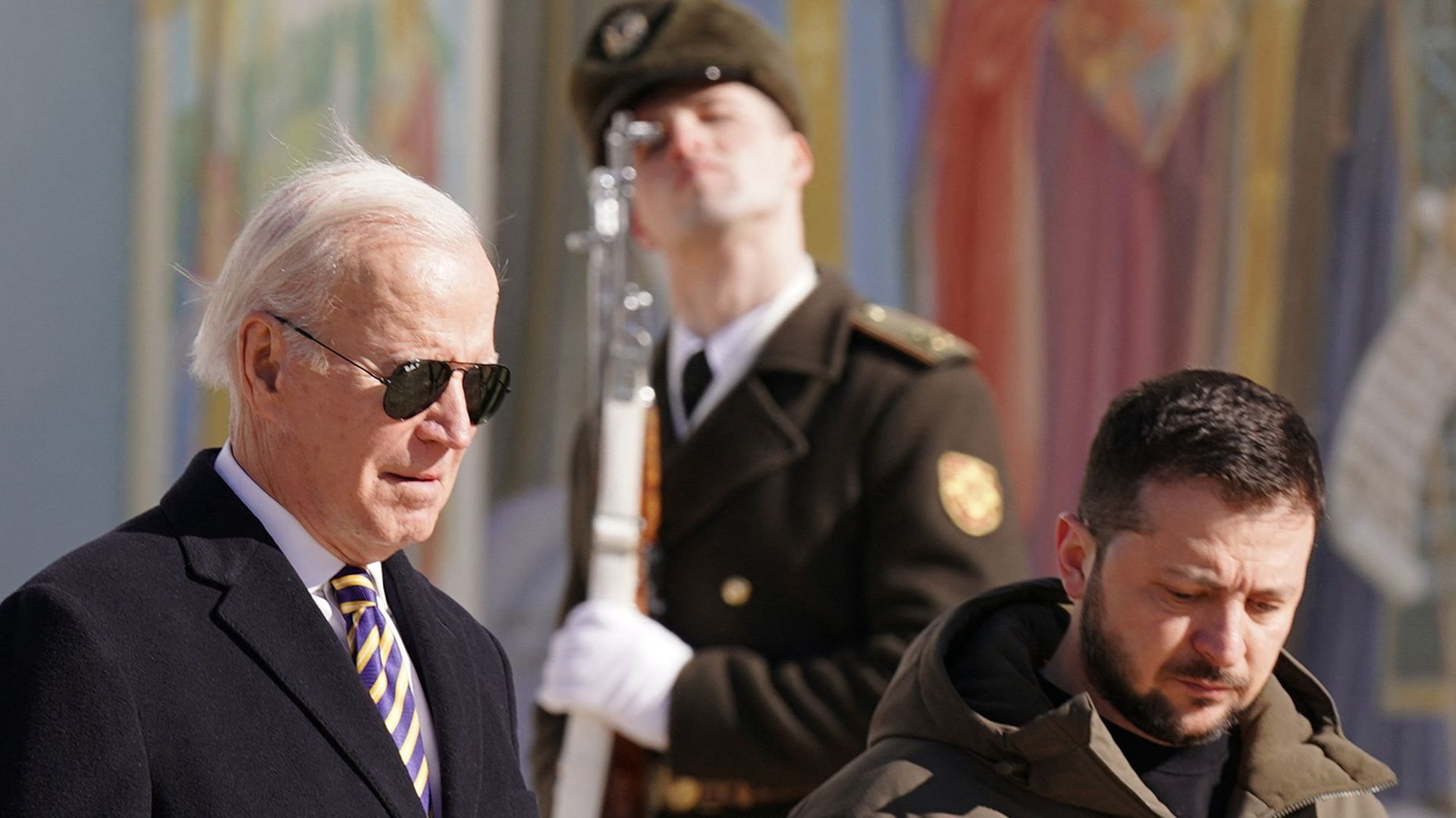 Le président américain Joe Biden (à gauche) marche à côté du président ukrainien Volodymyr Zelensky (à droite) devant une fresque religieuse à la cathédrale Saint-Michel à dôme doré, alors qu'il arrive pour une visite à Kiev le 20 février 2023.