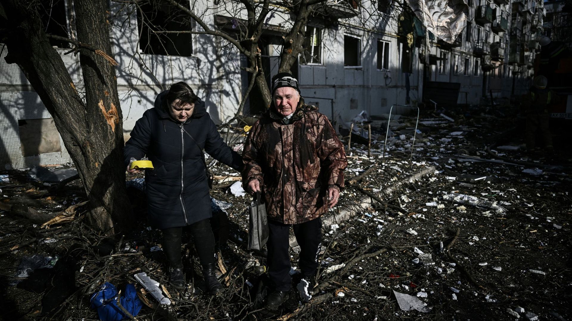 Des personnes passent devant le corps d'un parent à l'extérieur d'un bâtiment détruit après les bombardements sur la ville de Tchougouiv, dans l'est de l'Ukraine, le 24 février 2022. Les forces armées russes tentent d'envahir l'Ukraine depuis plusieurs di