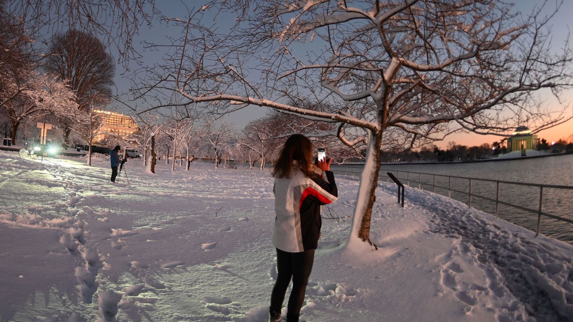 Une femme photographie le Jefferson Memorial à travers des arbres couverts de neige.