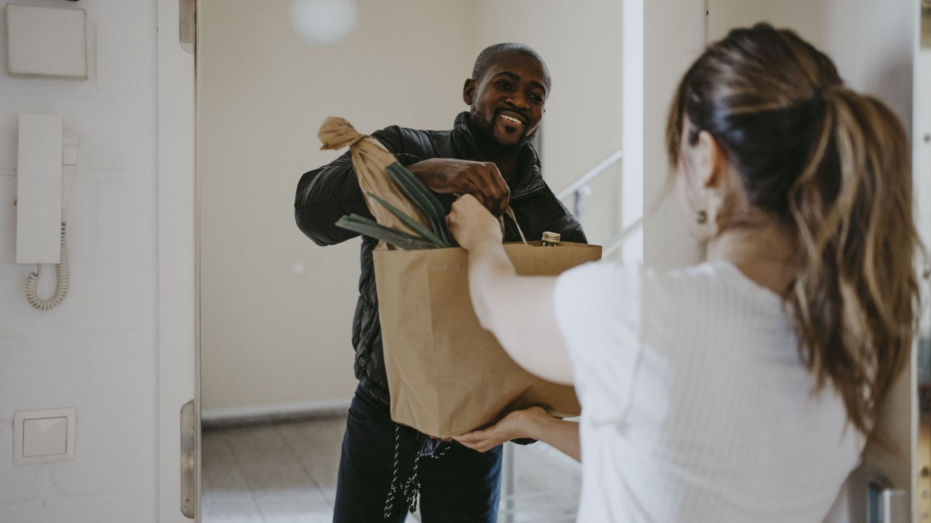 Smiling man giving paper bag of groceries to woman standing at doorway