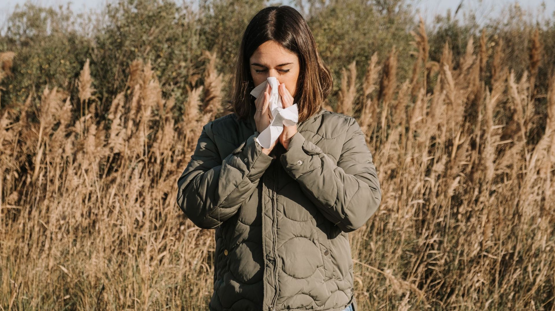 adult woman suffering spring allergy and blowing nose with a tissue in the nature