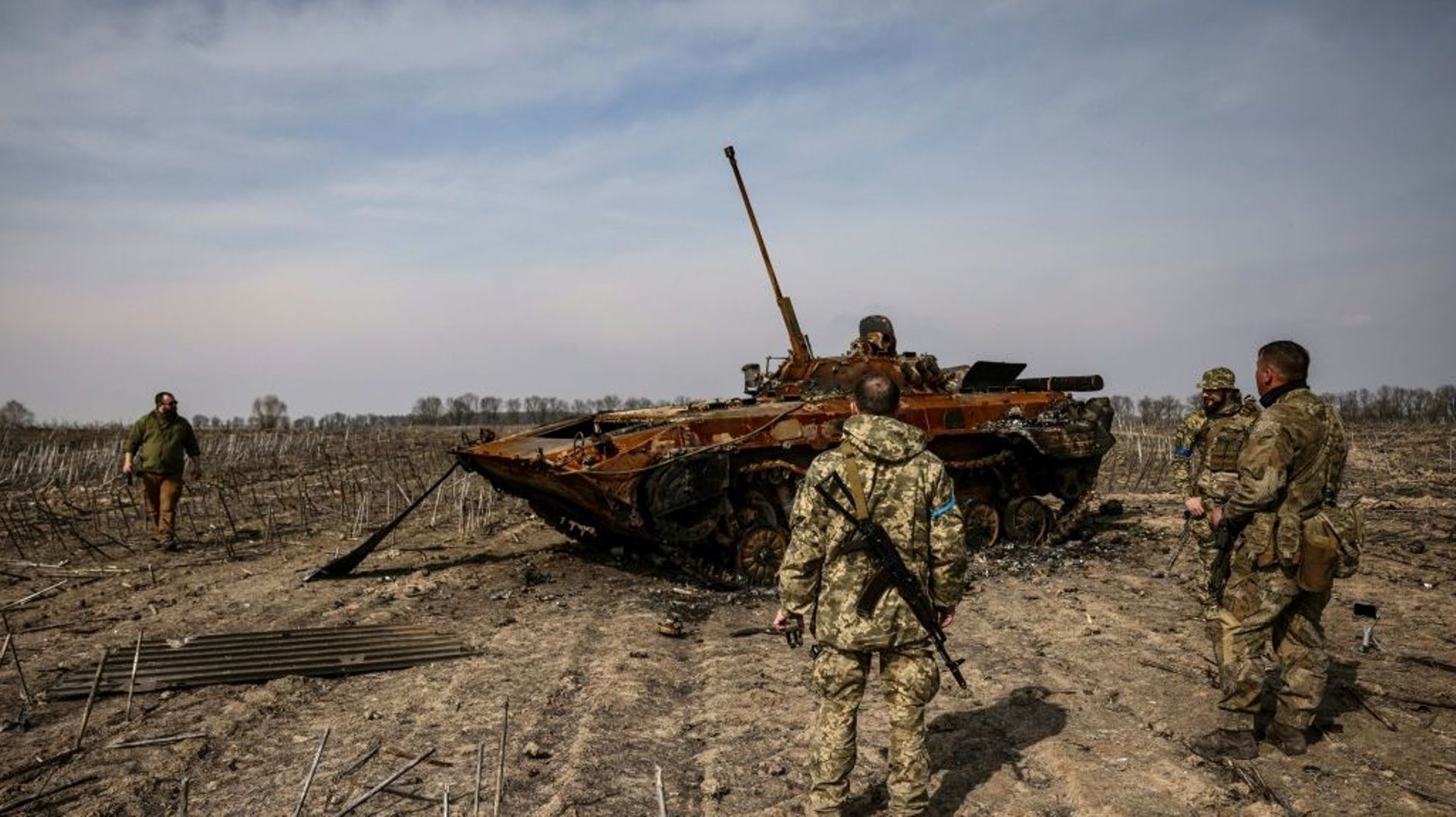 Des soldats ukrainiens se tiennent près d'un tank russe calciné le 31 mars 2022 dans la banlieue de Kiev