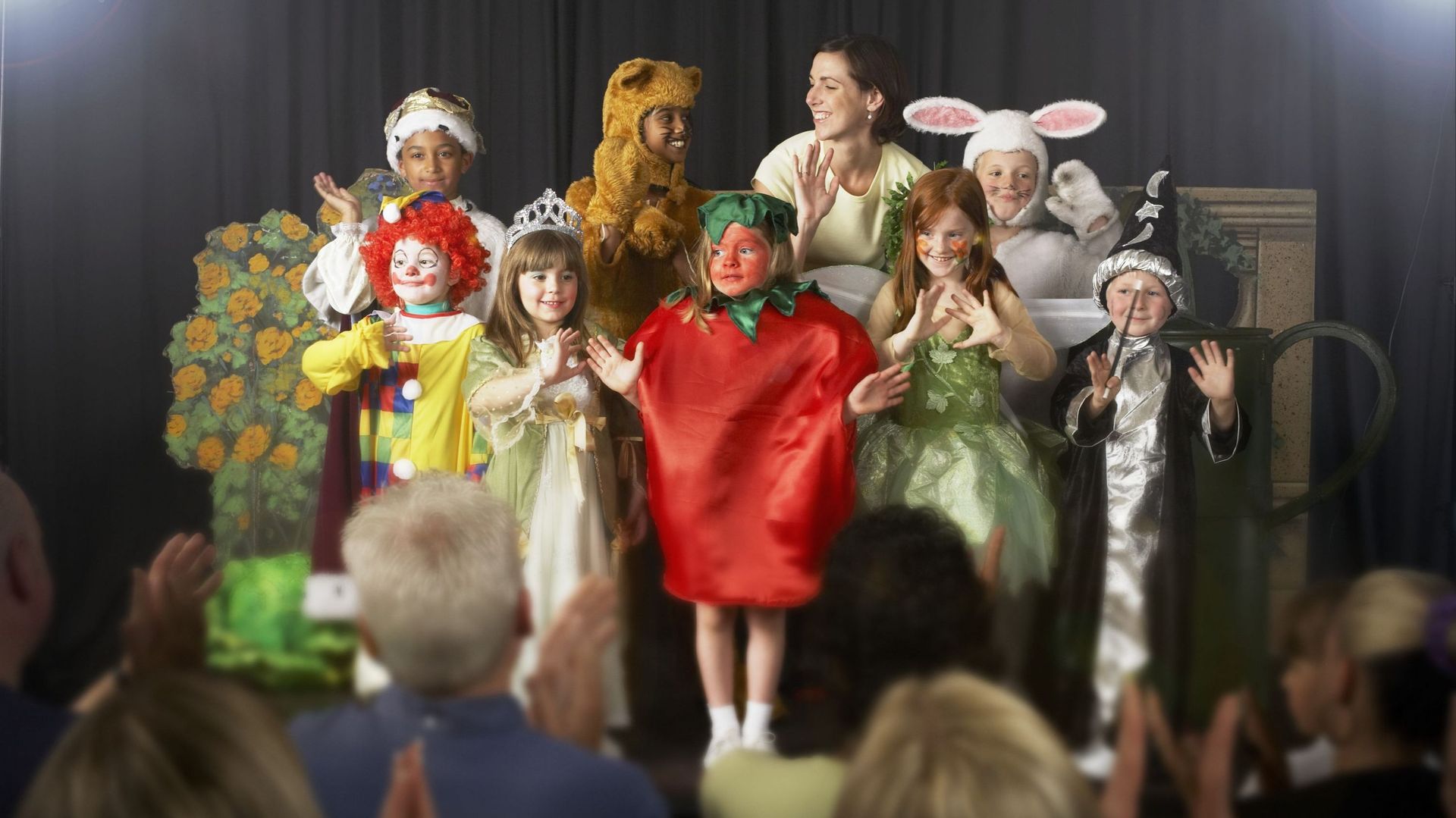 Children (4-9) wearing costumes and teacher waving on stage