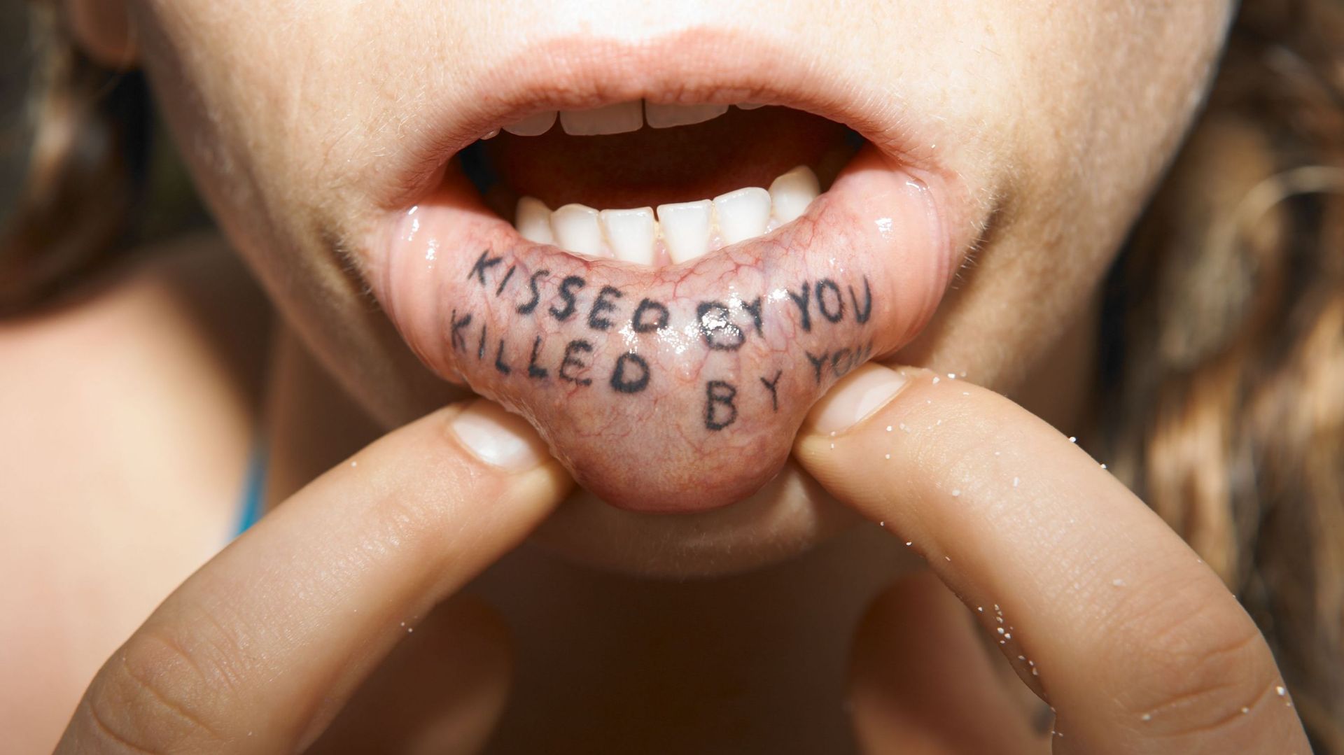 Kissed by you, killed by you tattooed on inside of woman&#39;s lip