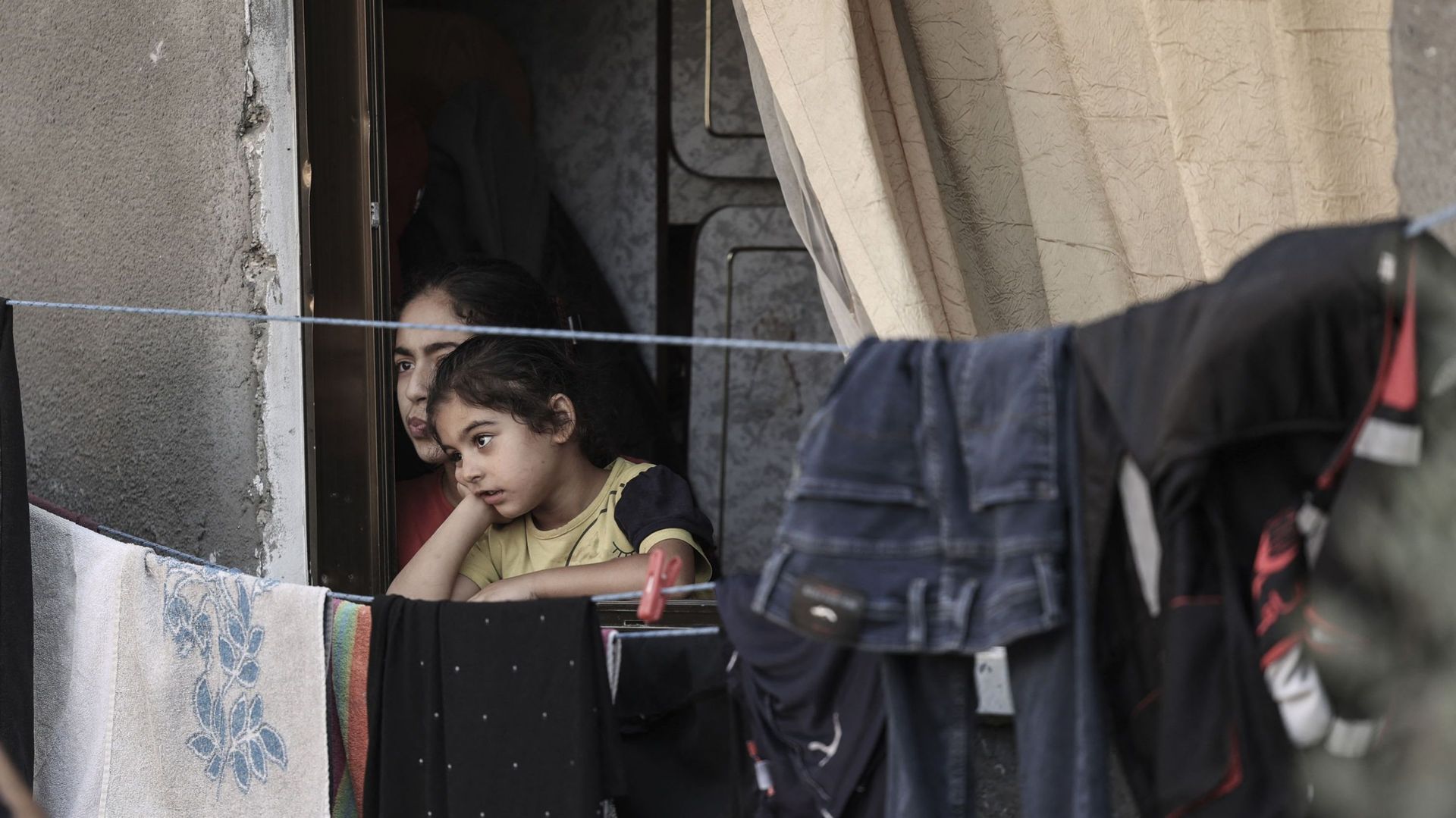 Des fillettes palestiniennes observent, le 8 août 2022, depuis leur balcon, des résidents qui évaluent les dégâts dans les zones touchées par les frappes aériennes israéliennes de la semaine dernière dans la ville de Gaza, après un cessez-le-feu proposé p