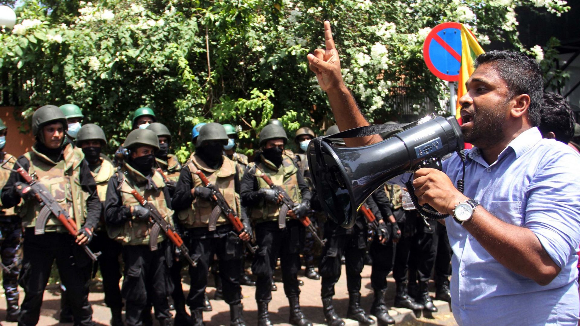 Un manifestant utilise un mégaphone alors que des militaires montent la garde devant le bureau du Premier ministre du Sri Lanka lors d’une manifestation antigouvernementale à Colombo, le 13 juillet 2022.